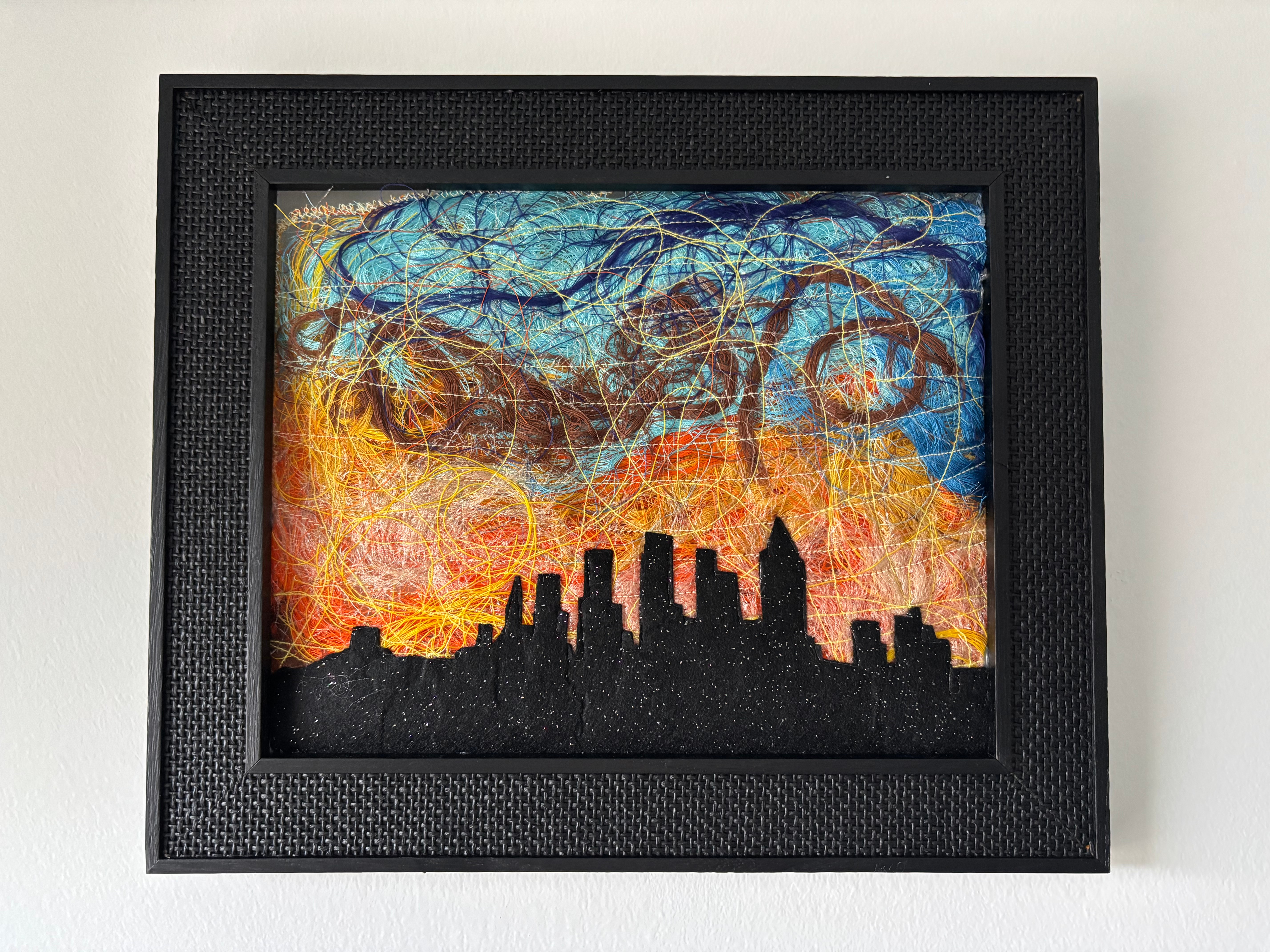Framed colorful abstract cityscape with swirling sky, silhouette of buildings, and vibrant sunset colors.