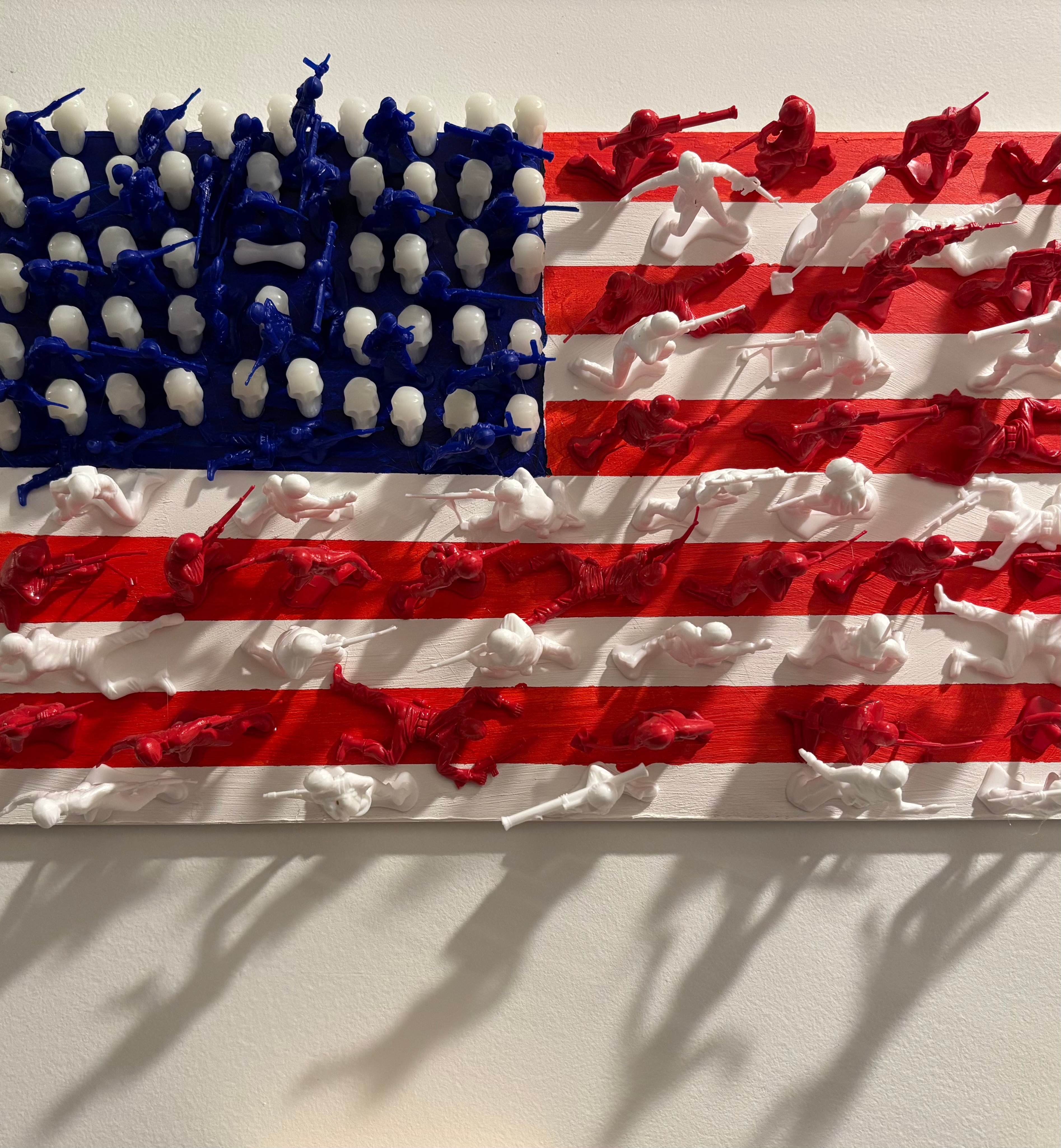 American flag made of candles with shadows on a wall, blue field with white stars, red and white stripes, 20 words