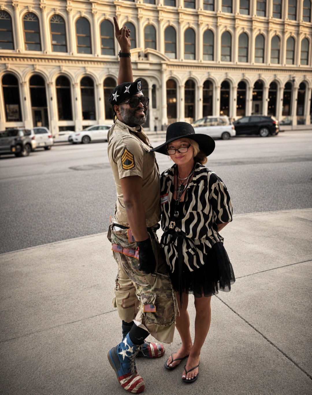 Two people standing on sidewalk in front of a historic building, one in military uniform, the other in a zebra-patterned dress and hat.