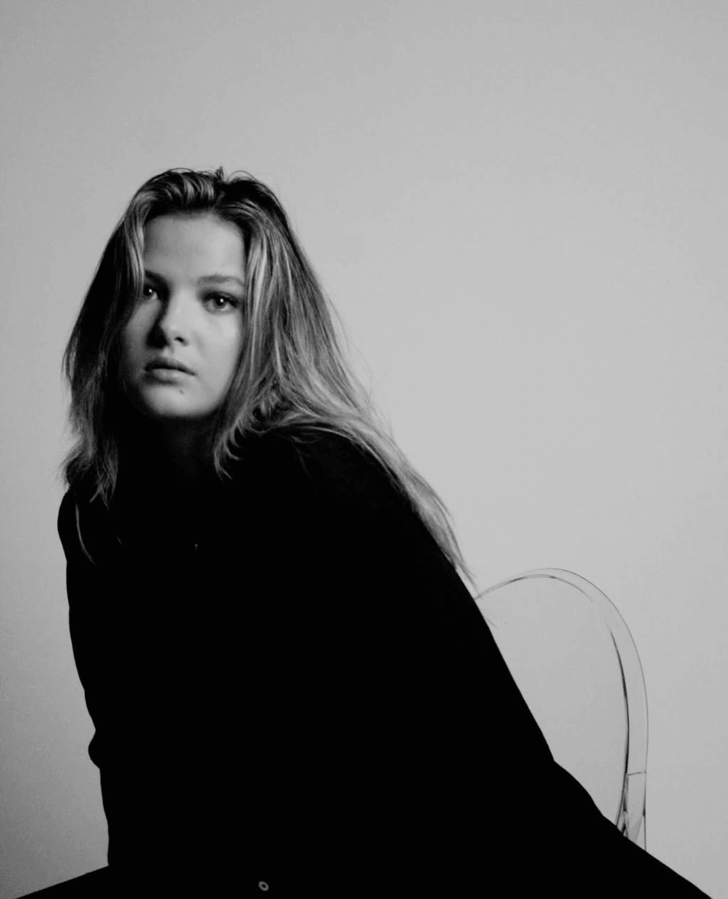 Black and white portrait of a woman with long hair, looking at the camera, against a plain background.