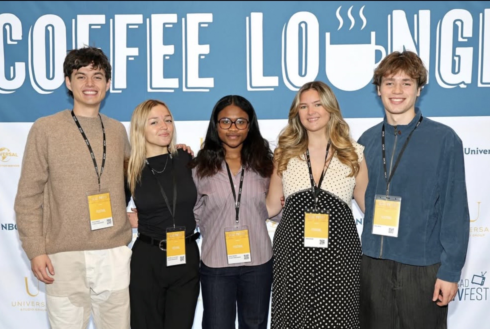 Group of five young people standing in front of a blue background with large white text, smiling, wearing name tags.