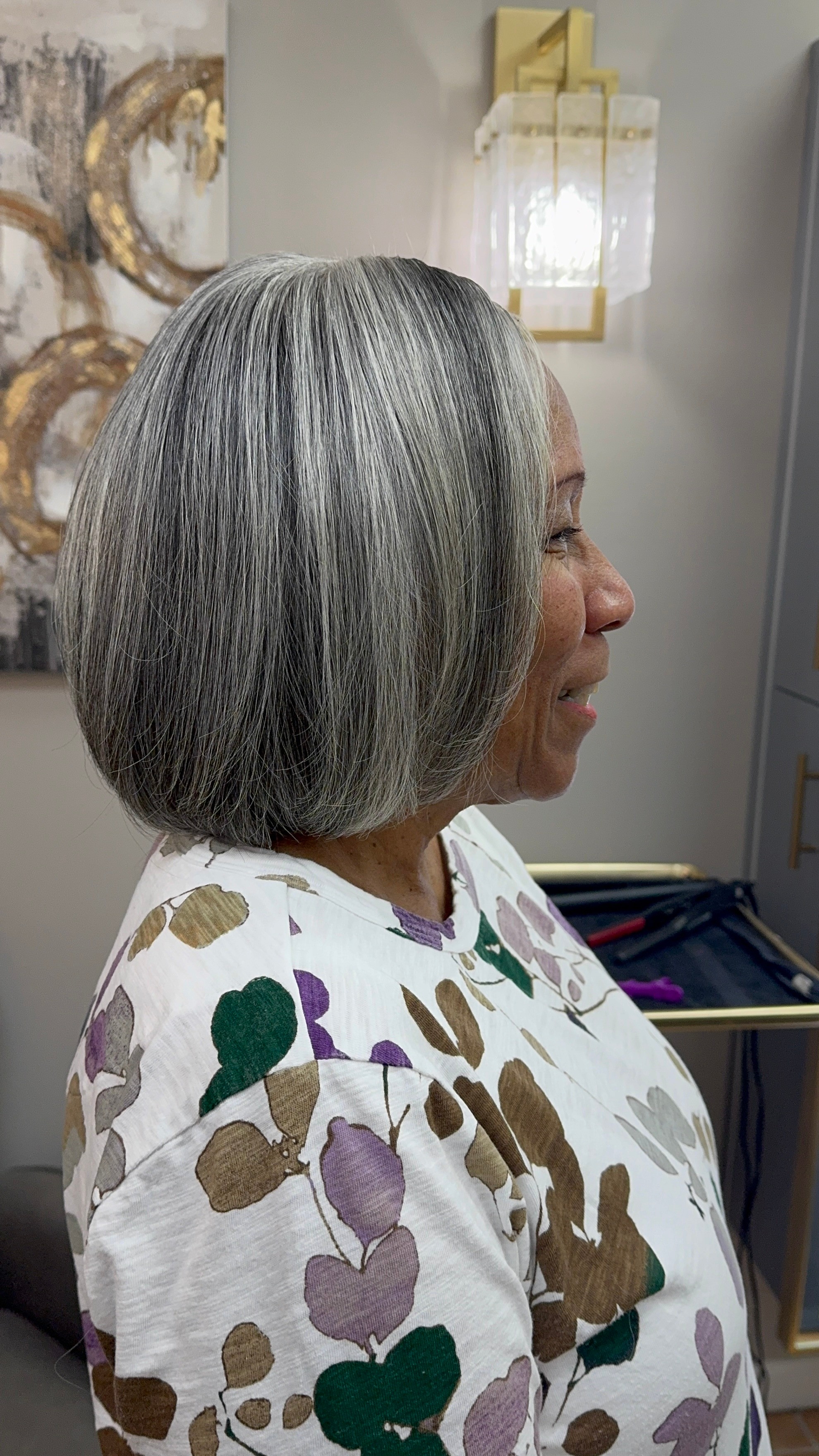 Profile of an older woman with gray hair in a bob style, wearing a patterned top, indoors.
