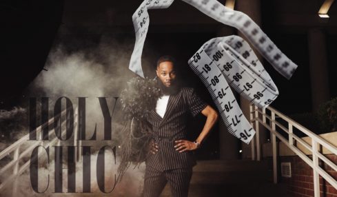 Person standing on a stage with a large paper roll, smoke, and red balls, in front of a sign reading 'HOLY CHIC'.