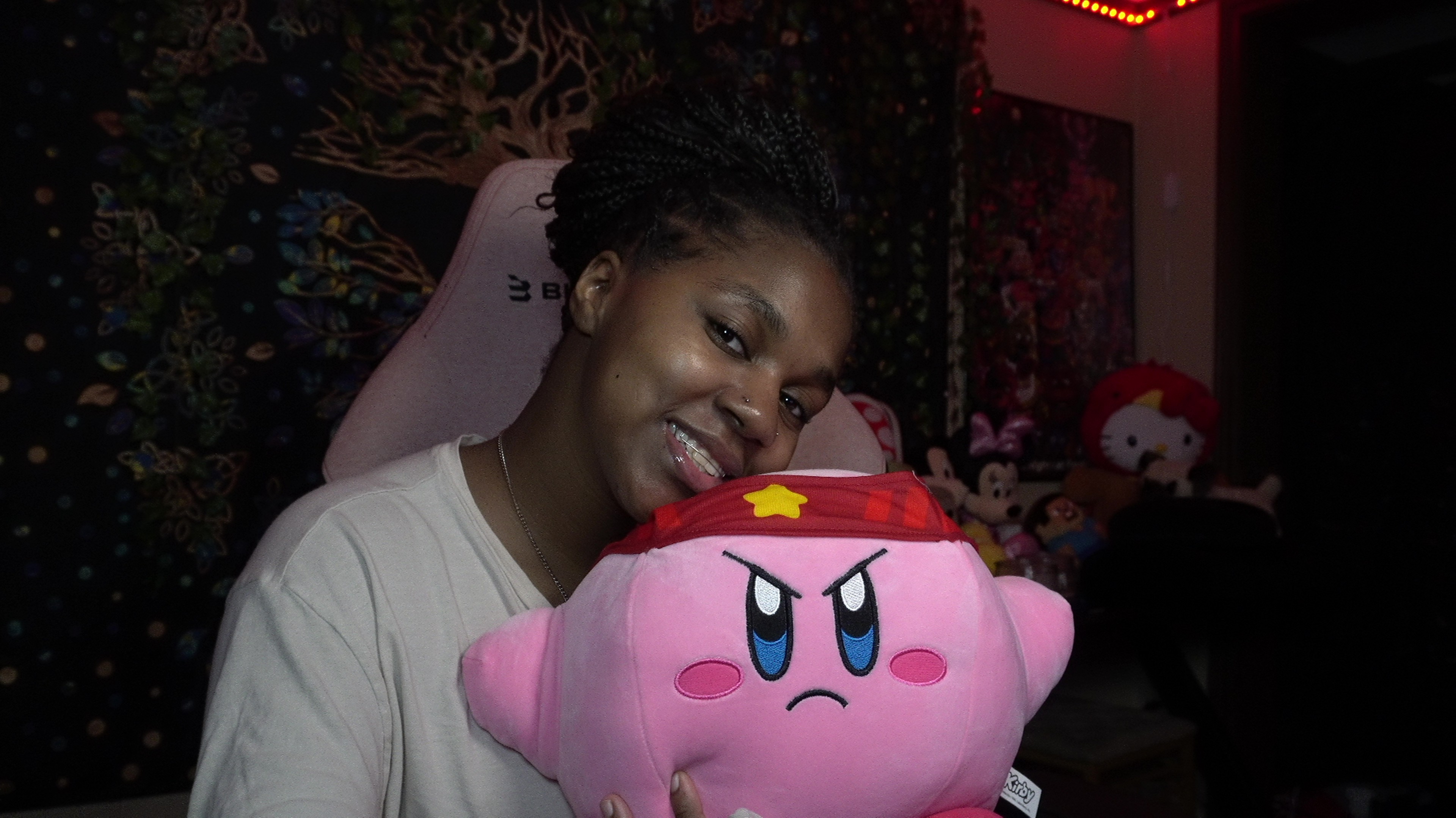 Young woman smiling with a pink plush toy character, in a dimly lit room with colorful decorations