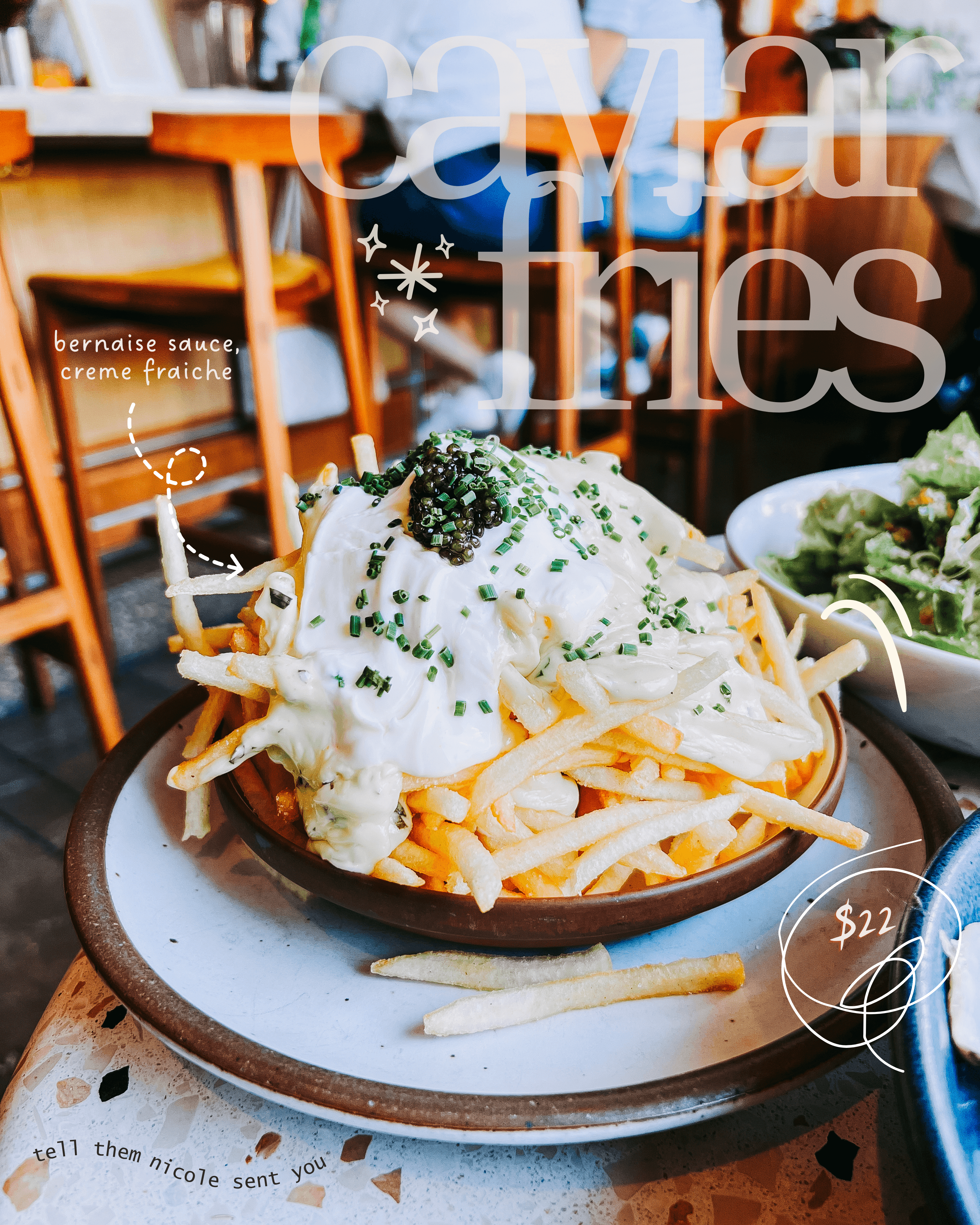Plate of fries topped with white sauce, green herbs, and broccoli, with a side salad in a bowl, in a restaurant setting.