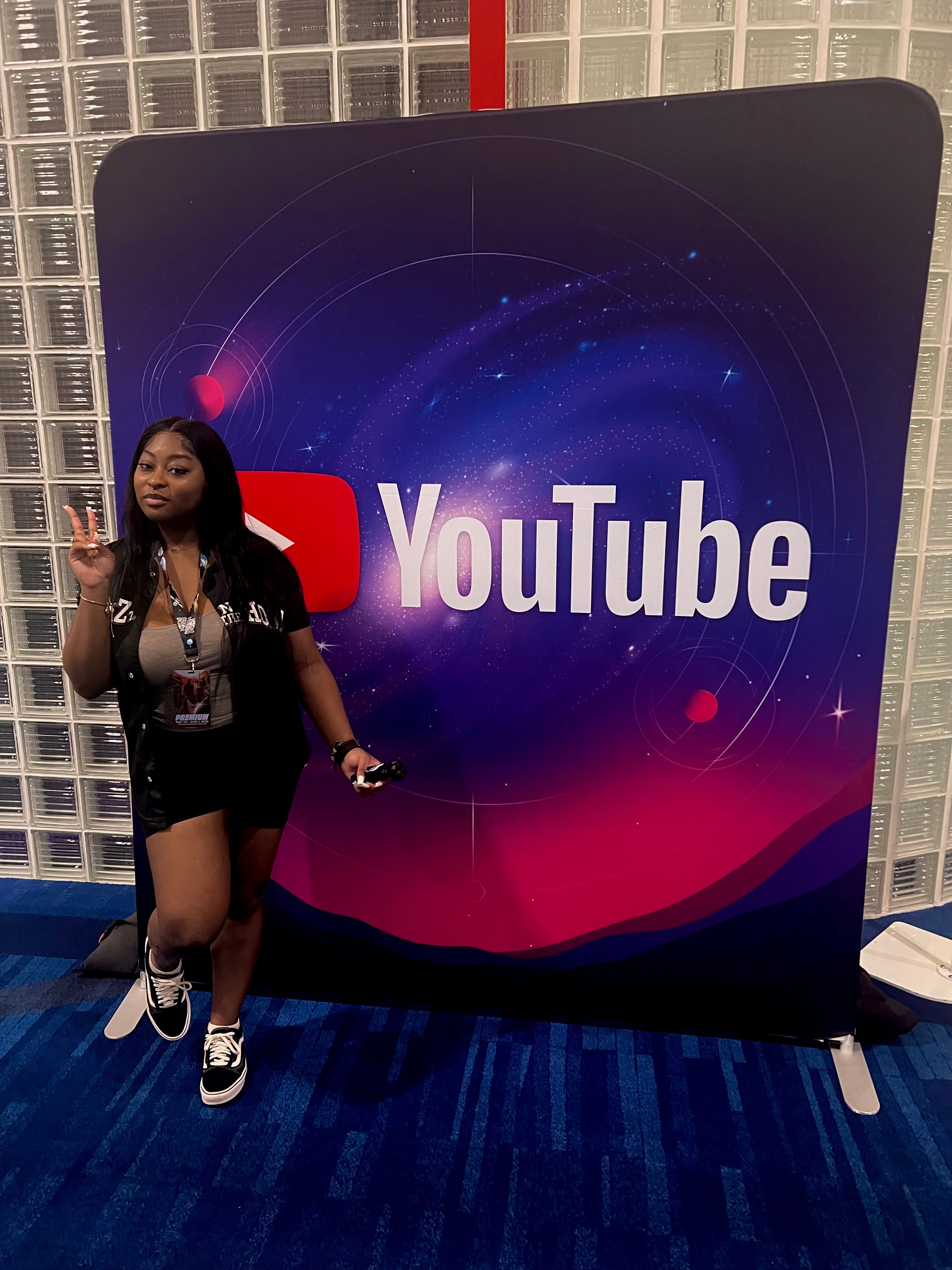 Person standing next to a large YouTube sign with a galaxy background, holding a phone, indoors.