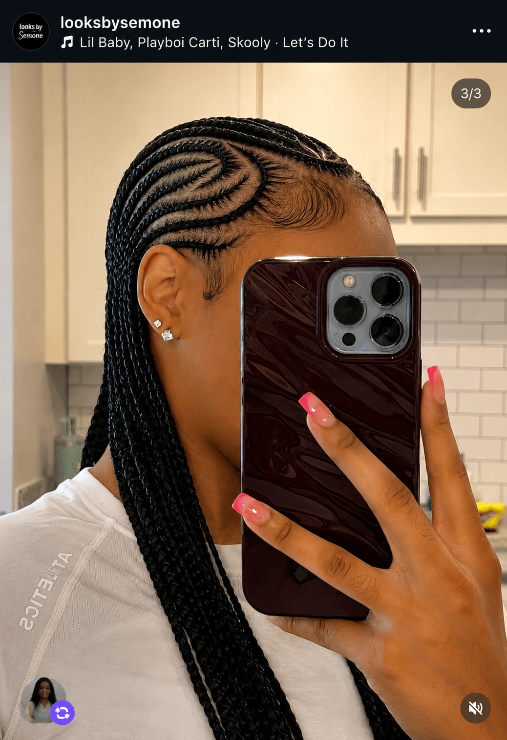 Person with braided hairstyle taking a mirror selfie, showing side of face and hand with pink nails, in a kitchen.