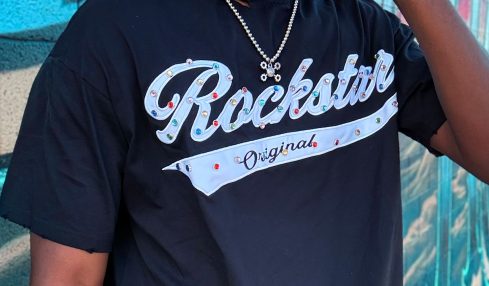 Man wearing sunglasses and a black T-shirt with 'Rockstar' text, standing in front of a colorful graffiti wall.