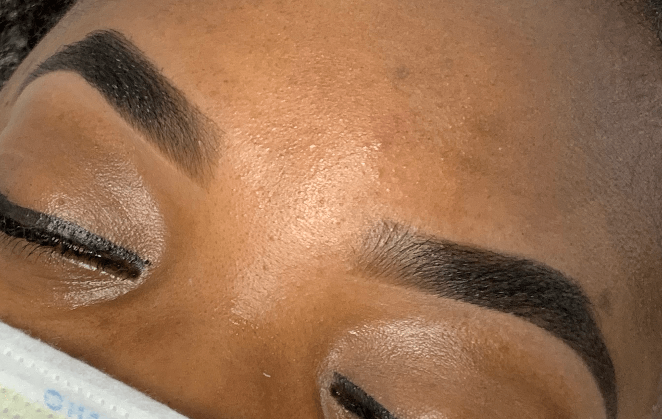 Close-up of a person's eyebrows and closed eyes, showing makeup and skin texture.