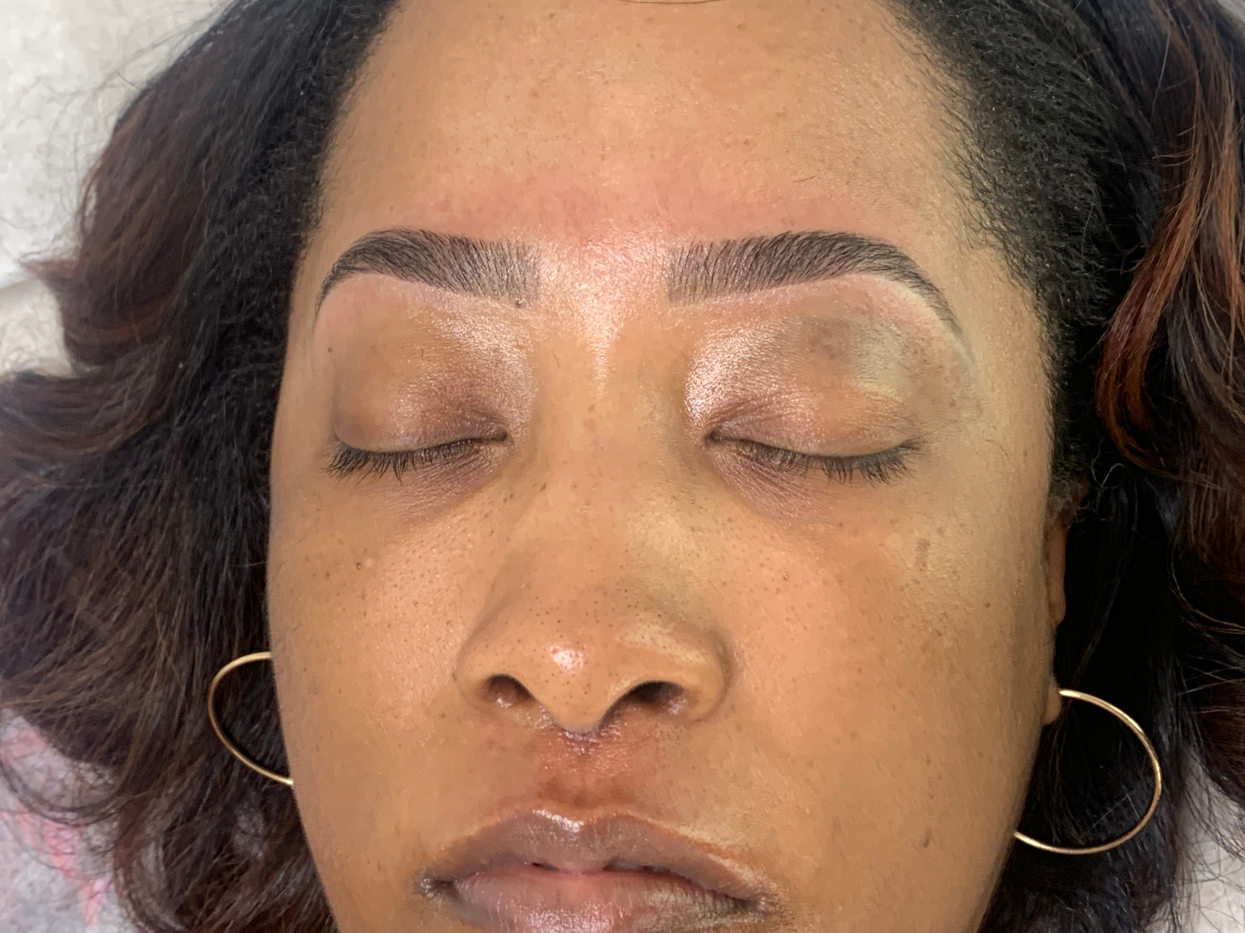 Close-up of a woman's face with closed eyes, showing eyebrows, eyelids, and lips, with earrings visible.