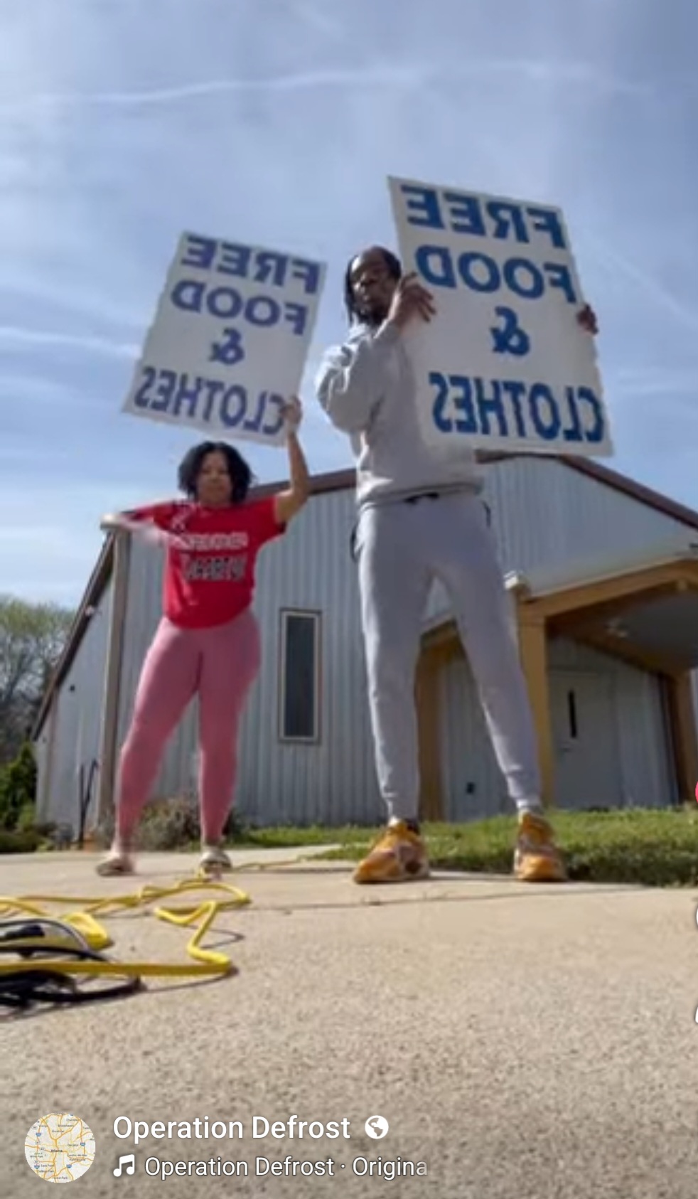 Two people holding signs that say 'FREED FOOD & CLOTHES' outside a building, with a clear sky in the background.