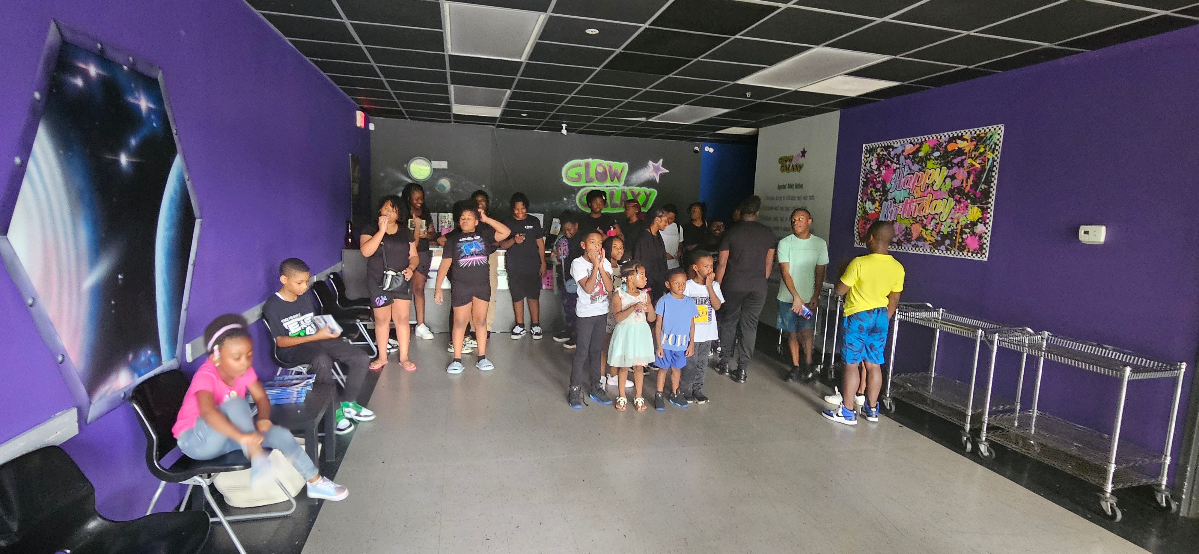 Group of children and adults gather in a purple-walled indoor play area with colorful decorations and artwork.