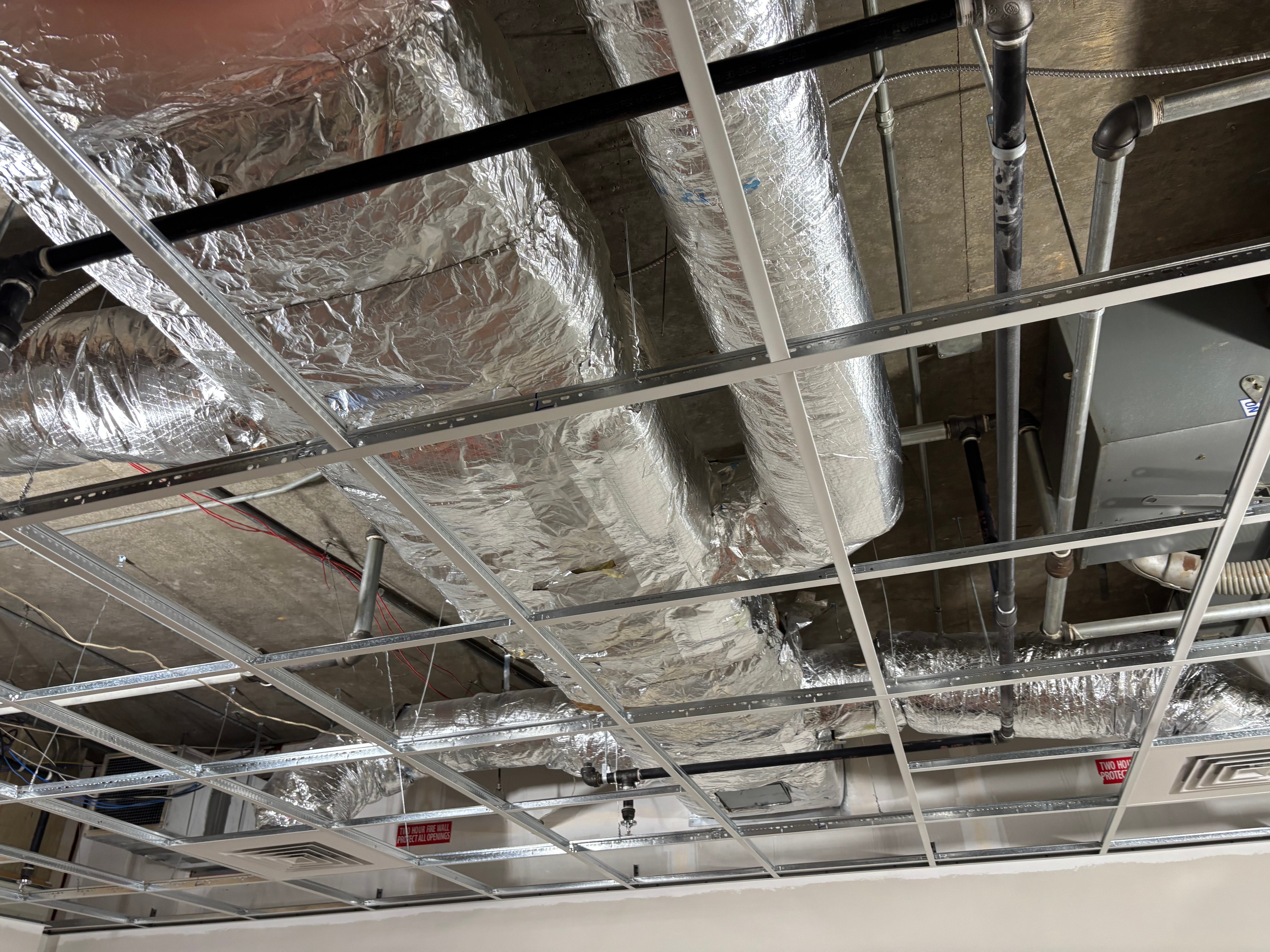 Ceiling with exposed ductwork and metal grid structure, with pipes and electrical components visible.
