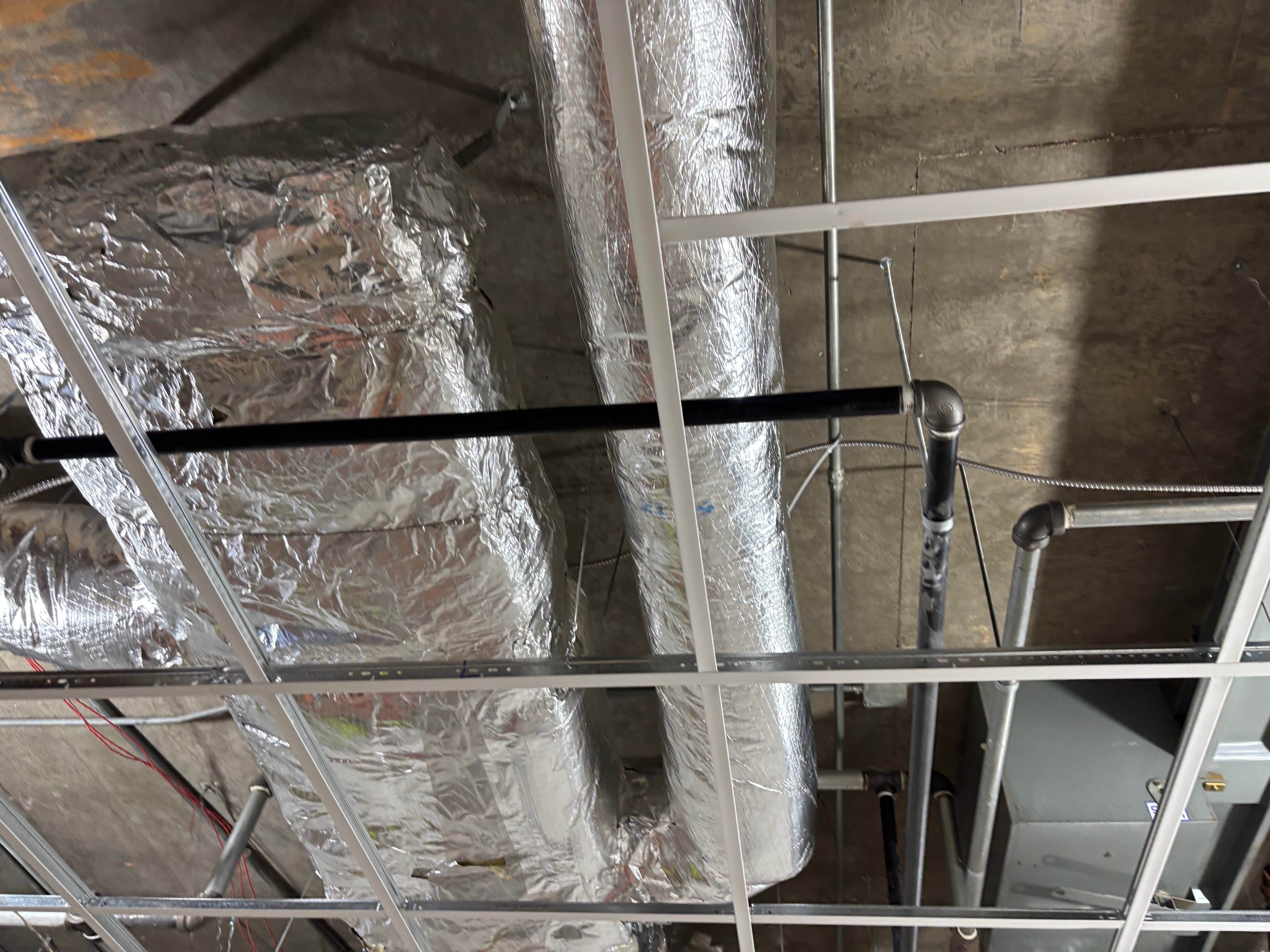 Ceiling with metallic ducts and pipes, viewed from below, with grid structure overhead.