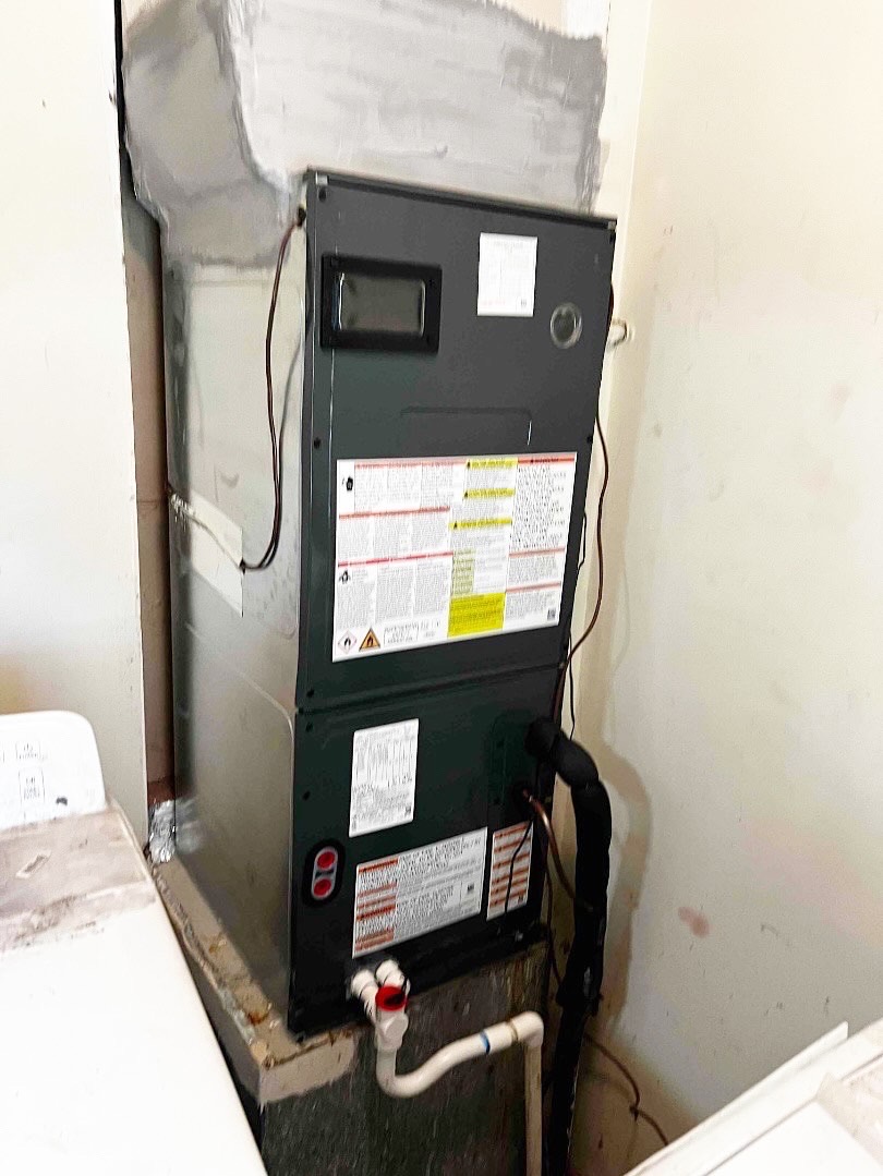 HVAC unit installed in a wall niche with exposed pipes and wiring, against a partially unfinished wall.