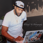 Man wearing a white cap and t-shirt, working on a laptop decorated with stickers, in front of a cityscape background.