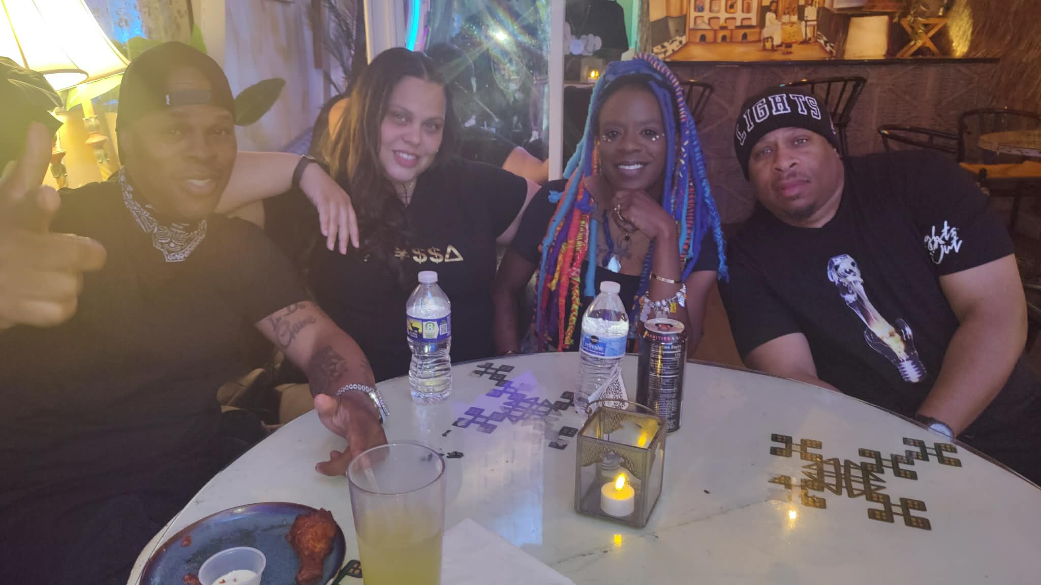 Four people sitting at a table with drinks, smiling, in a dimly lit setting.