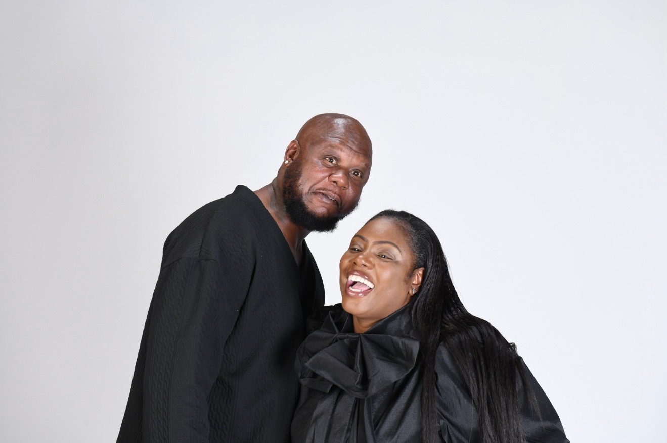 Two people smiling and leaning close together against a plain white background.