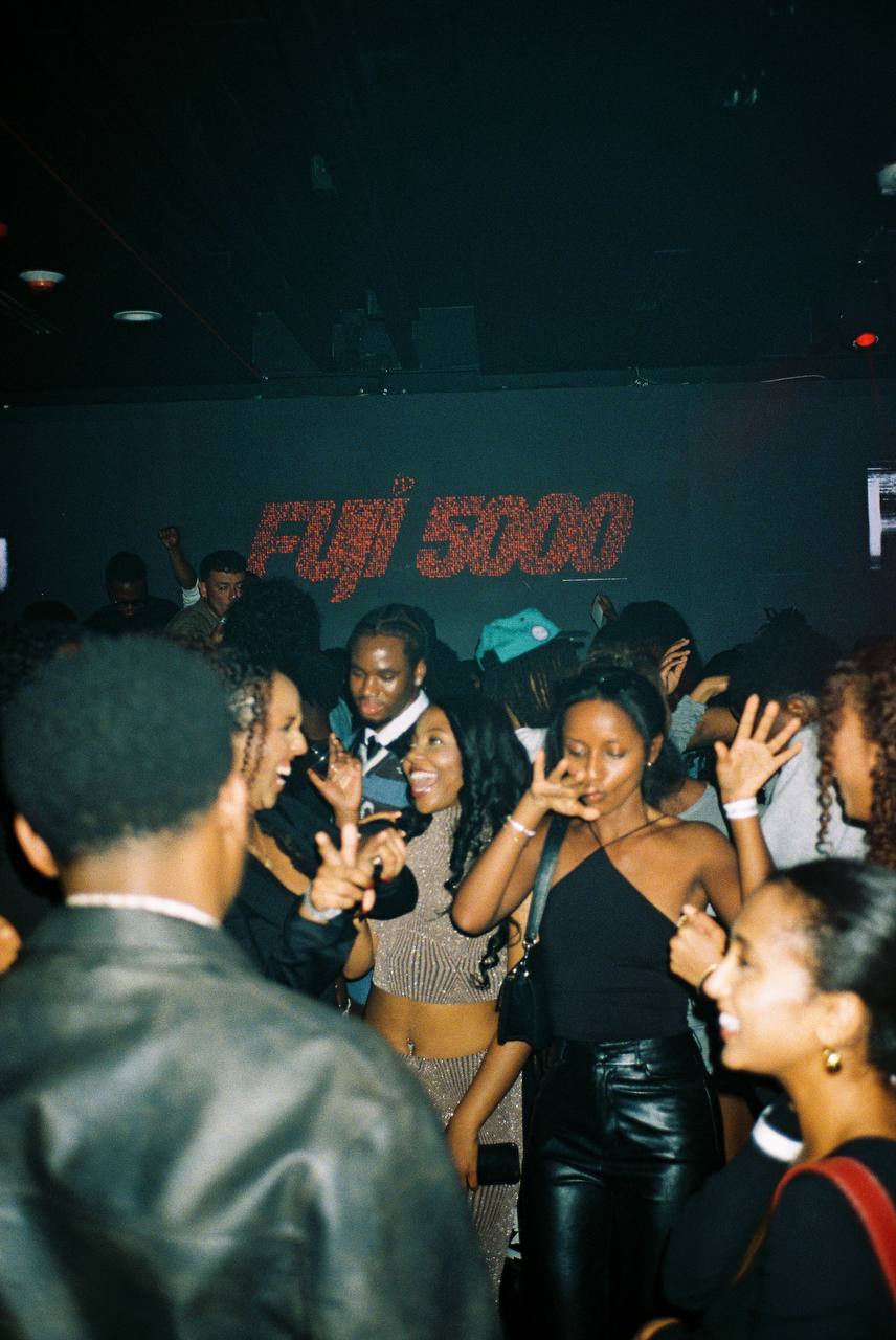 Group of people dancing and socializing at a party with a large screen displaying 'EJJI 500' in the background.