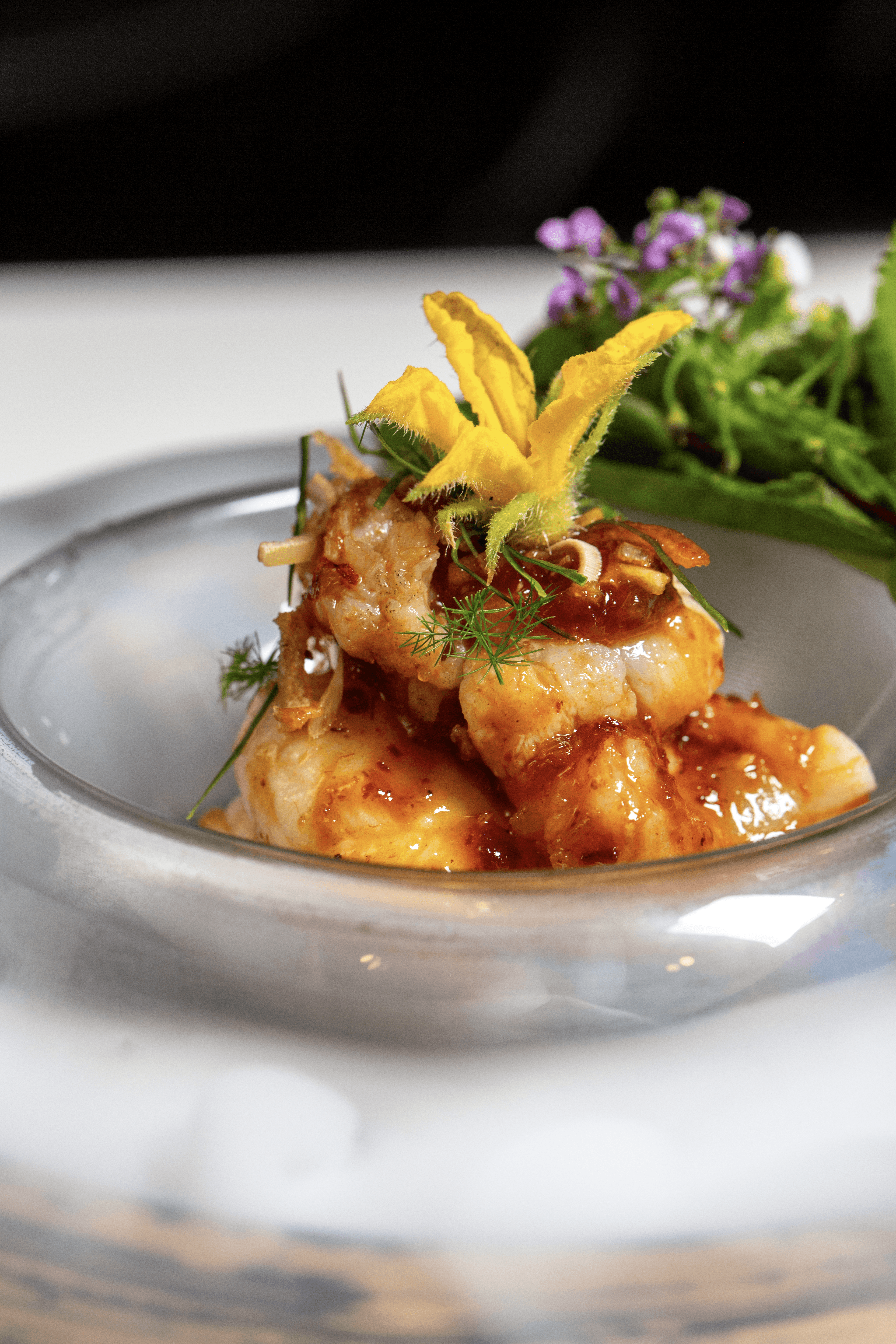 Close-up of a plated dish with fried food topped with herbs and garnished with yellow and purple flowers, on a white plate.