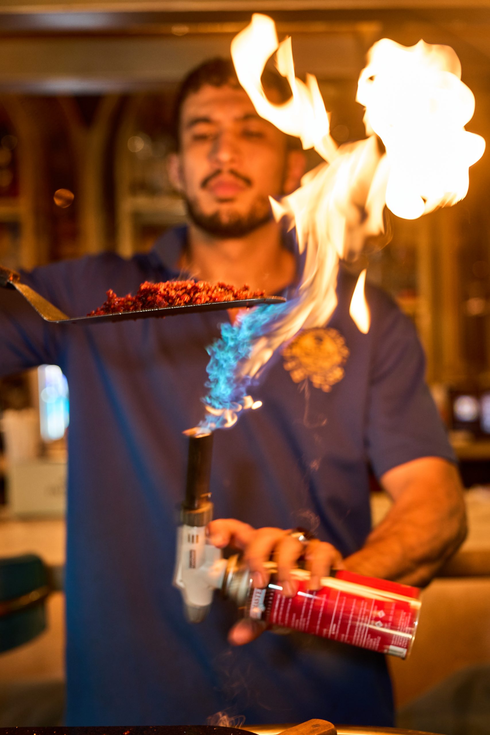 Person holding a flaming torch with fire and smoke, in a dimly lit environment.