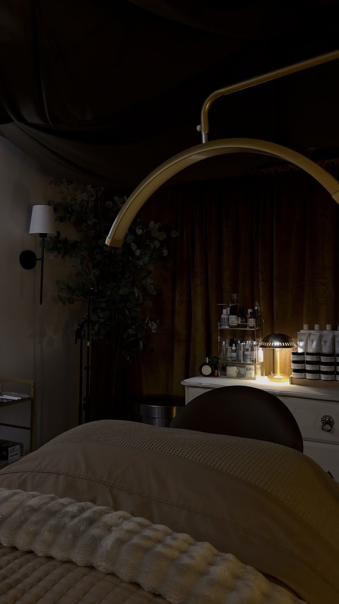 A dimly lit room with a bed, a large gold-colored lamp, and a bar cart with bottles and glasses.