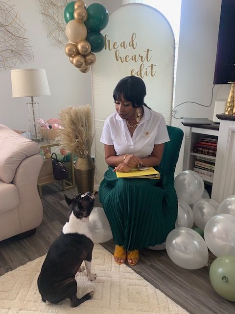 Person sitting on a chair with balloons around, reading a book, in a room with a bookshelf and a lamp.