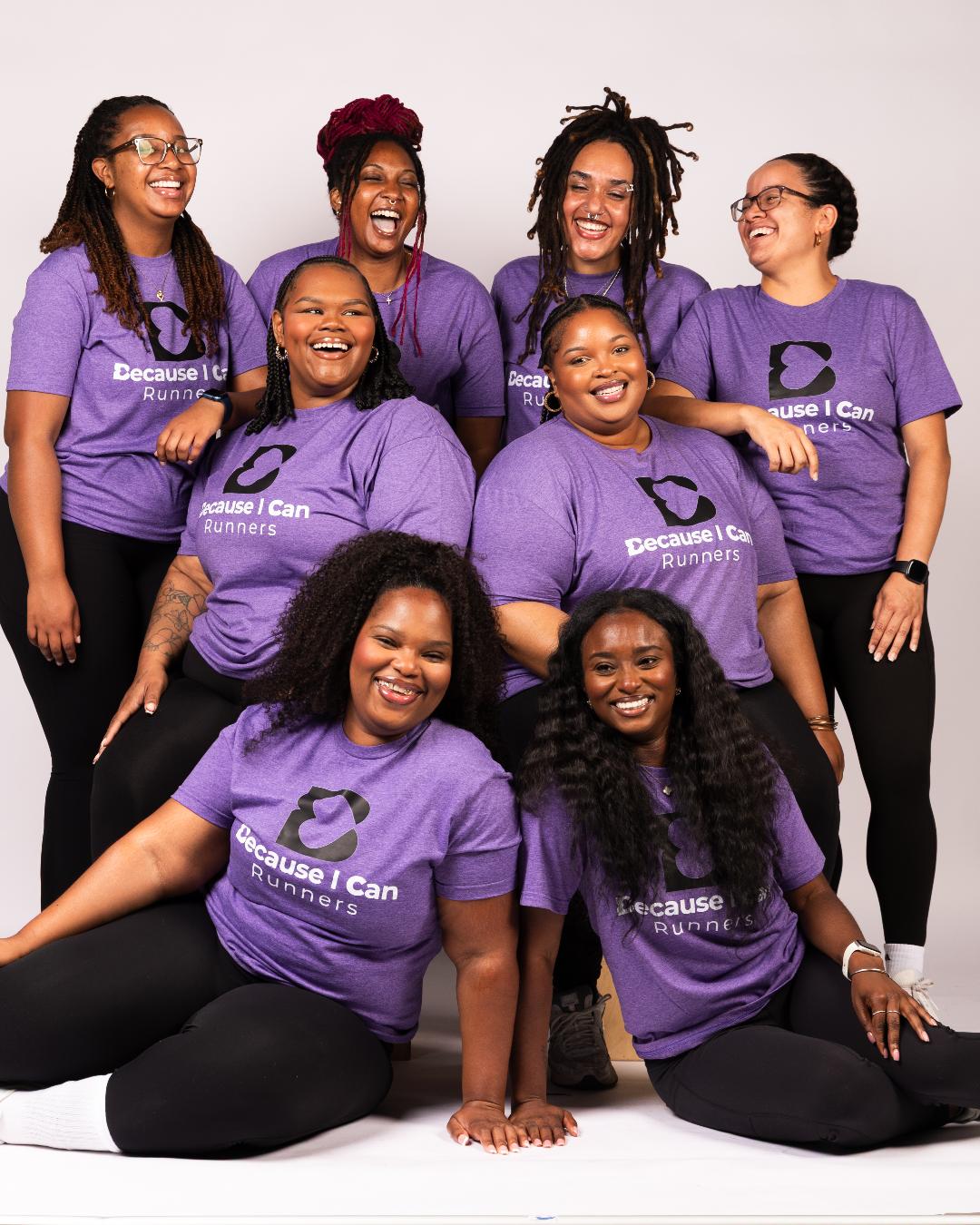 Group of eight women wearing matching purple shirts, smiling and posing together against a white background.