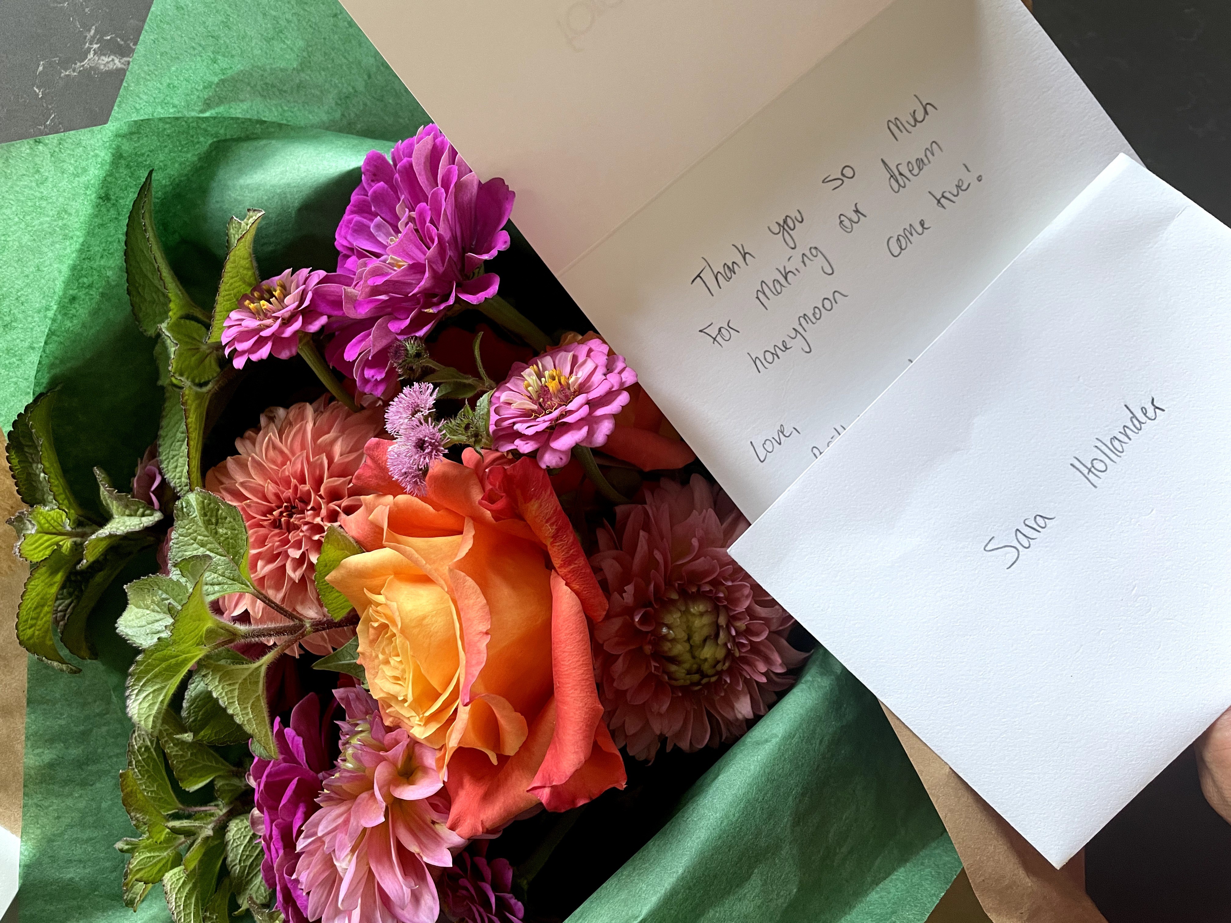 Colorful bouquet of pink, orange, and purple flowers with green leaves, accompanied by a handwritten note and a printed note.
