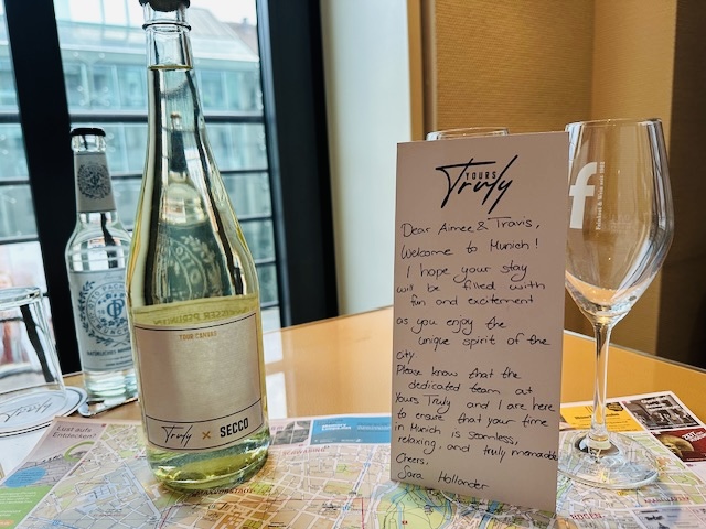 A glass bottle of sparkling water, a wine glass, and a handwritten note on a table near a window.