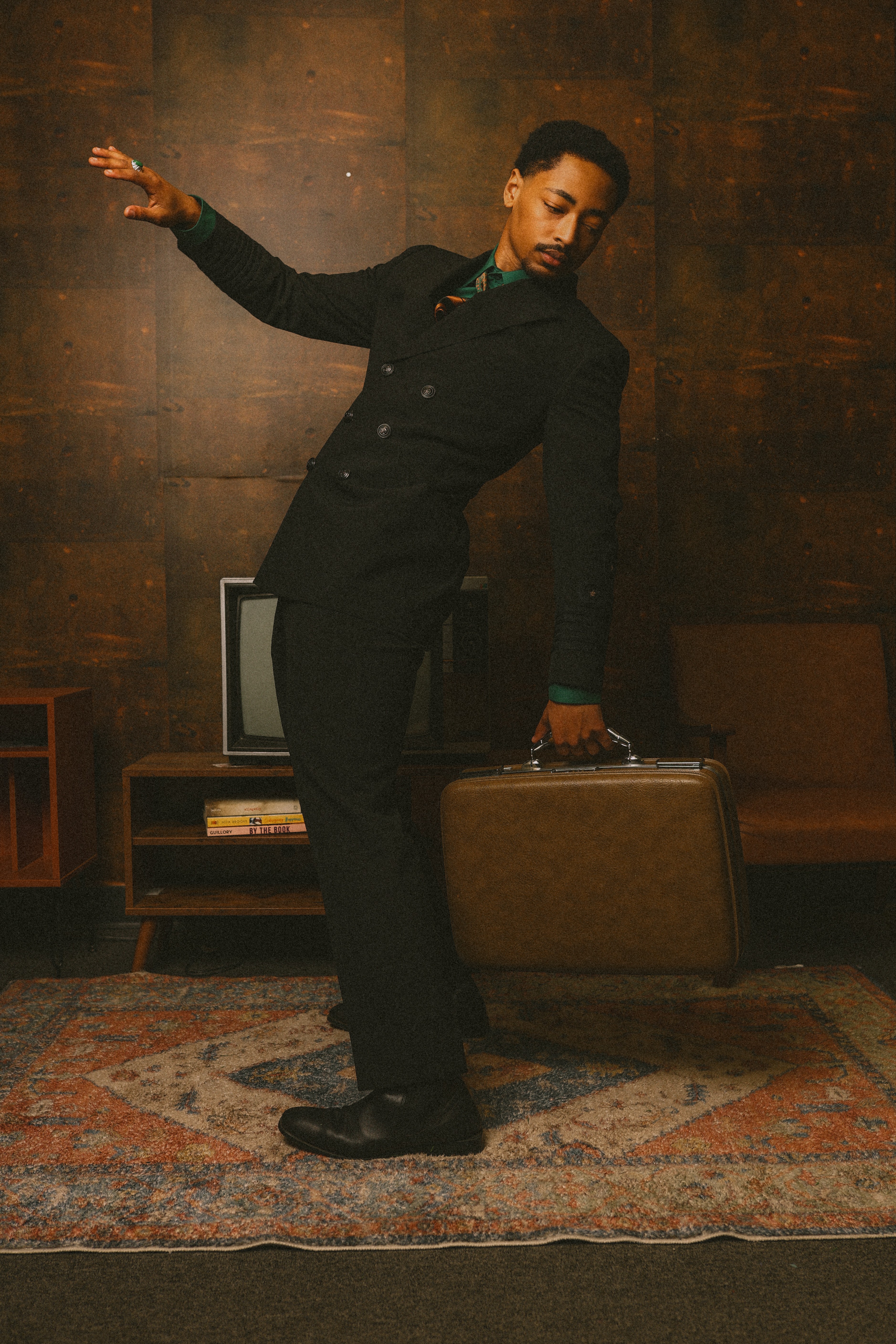 Person in black suit dancing in a room with wooden walls and vintage furniture.