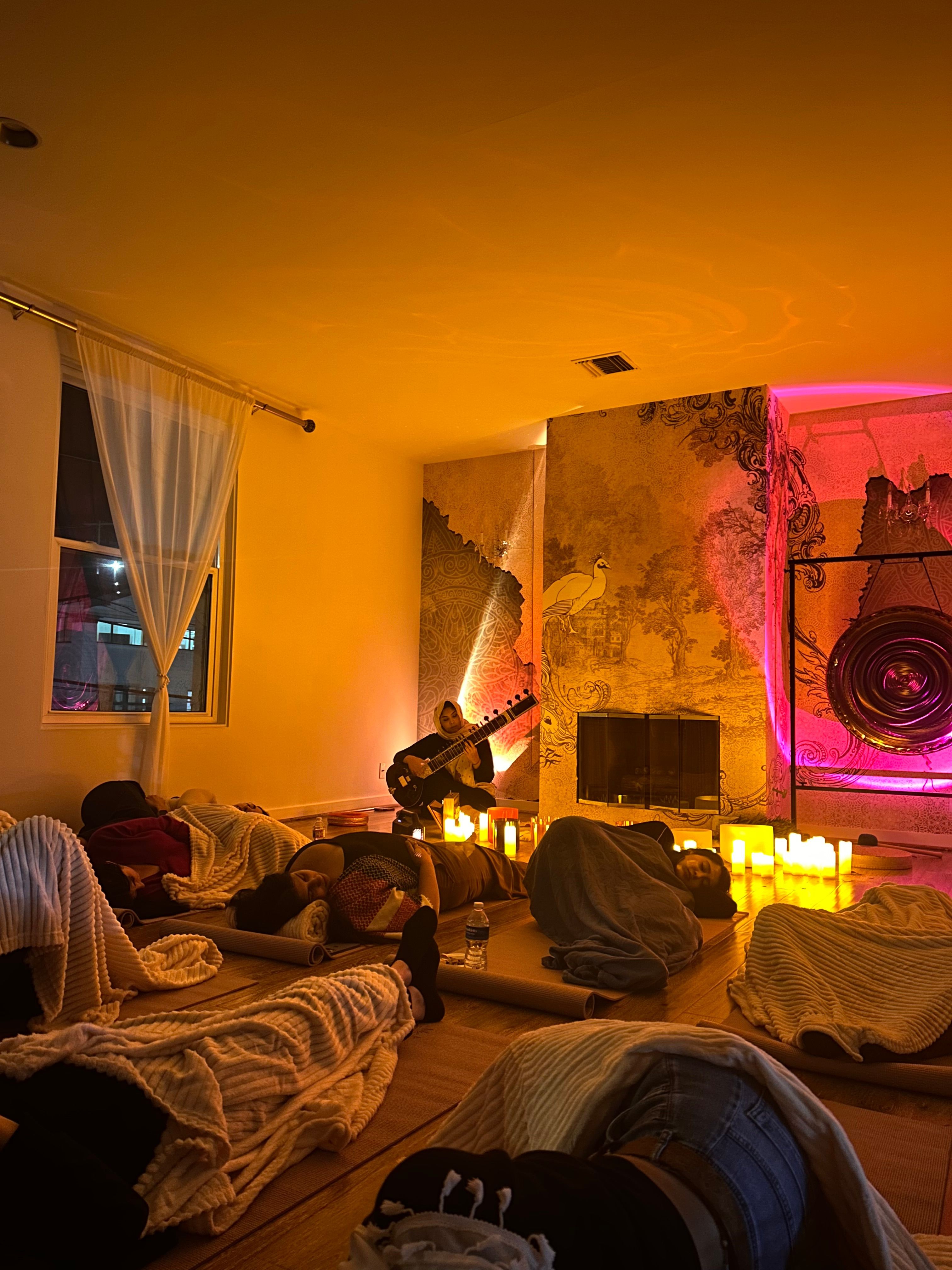 People sitting in a room with colorful lighting, some facing a wall with a window, others at a table, relaxed atmosphere.