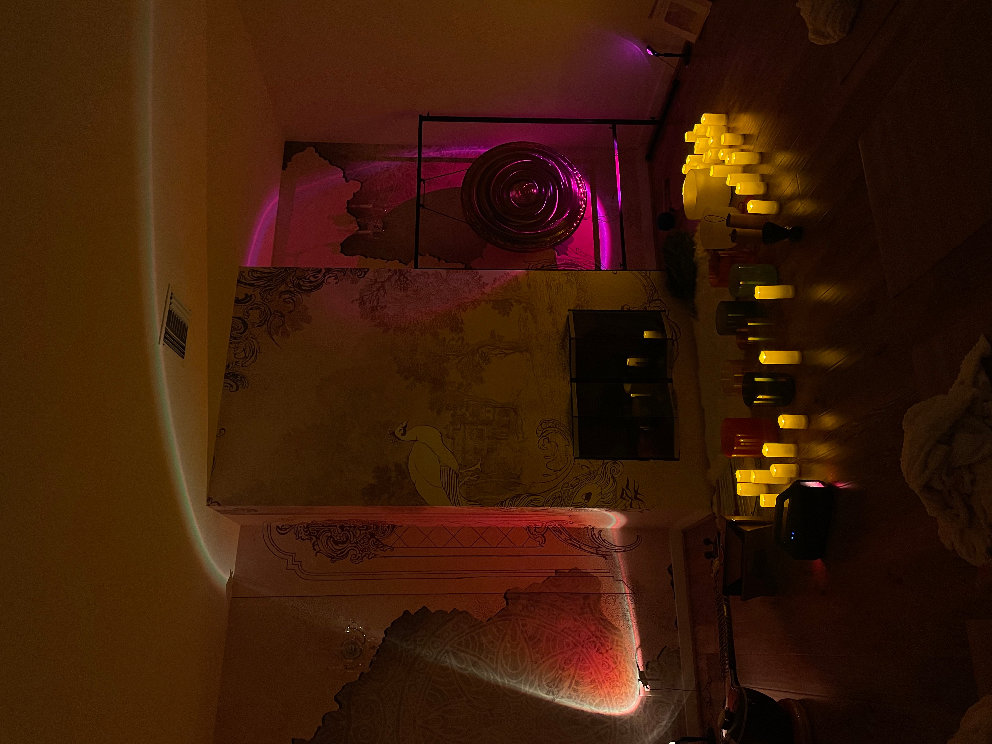 Upright view of a room with pink and yellow lighting, a wall with candles, and a decorative wall feature.