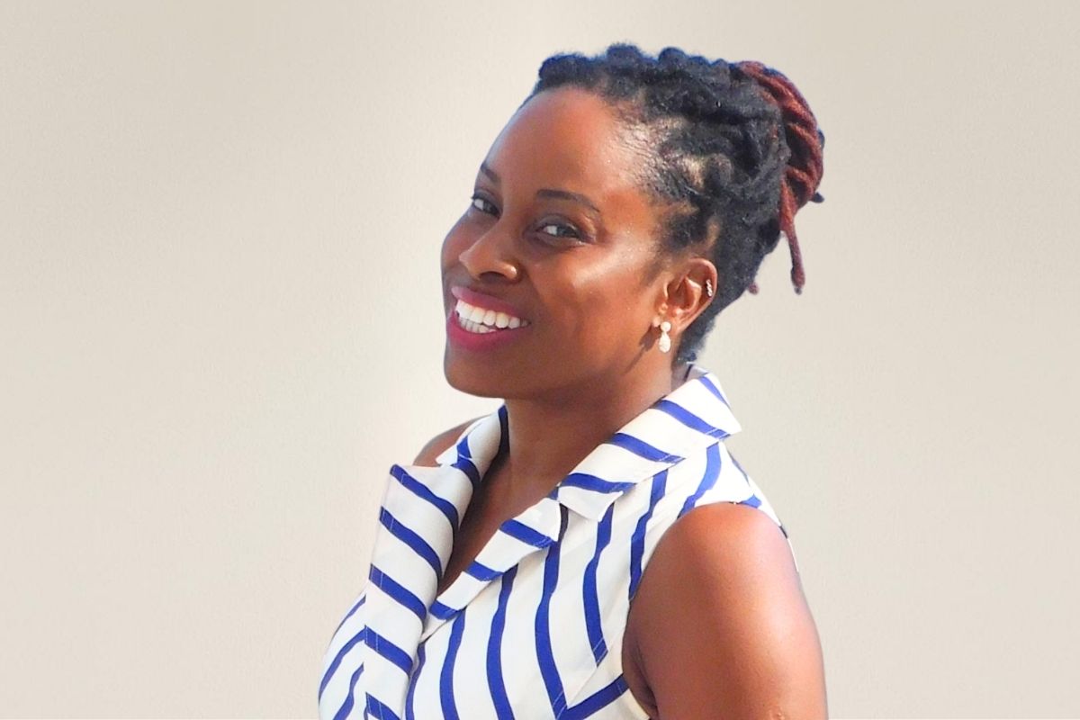 Woman with braided hair smiling, wearing a striped sleeveless top, against a plain background.