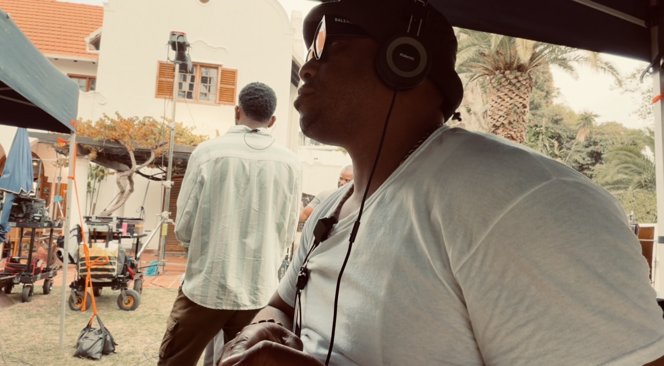 Person wearing headphones and sunglasses, sitting outdoors with a market scene in the background.