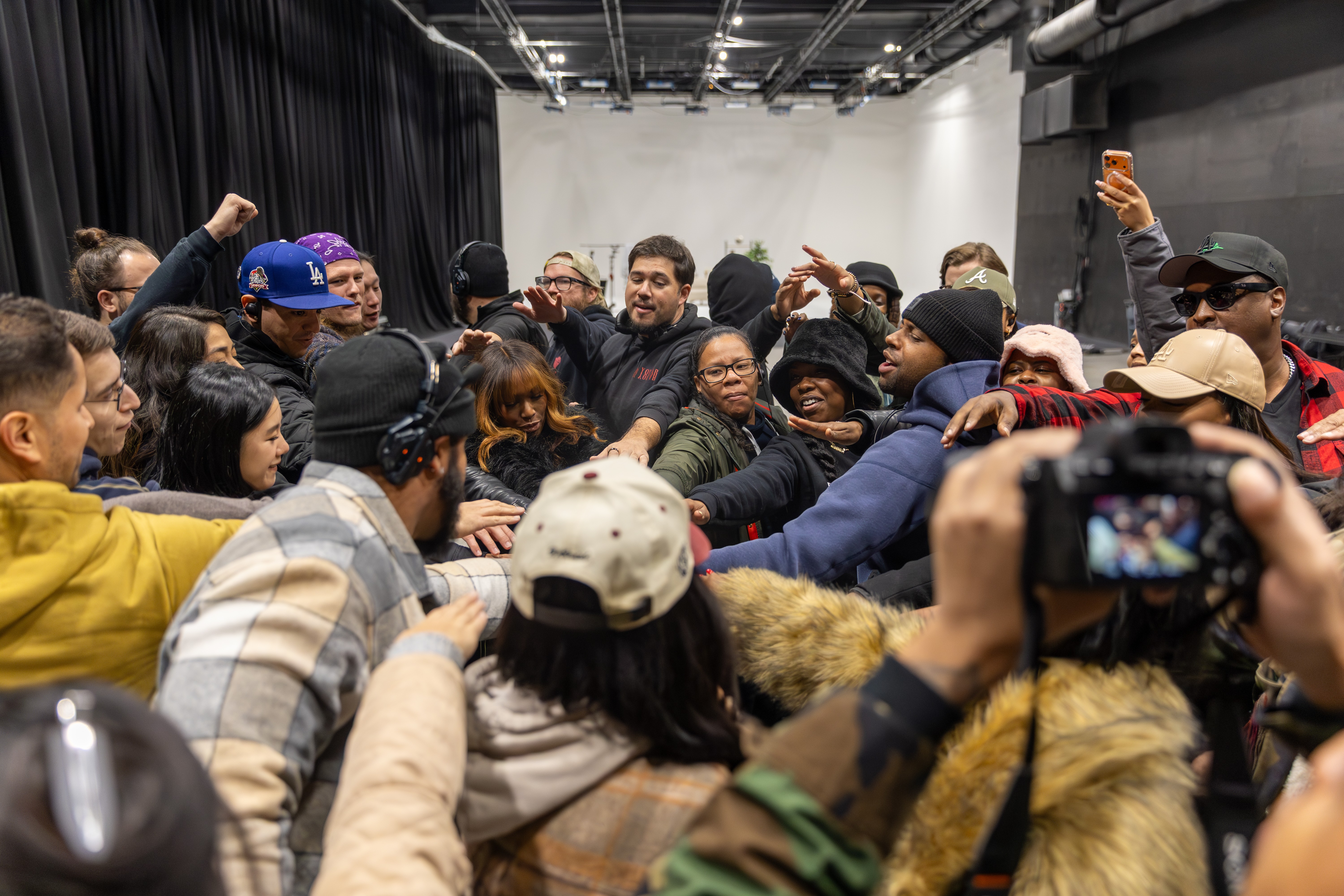 Group of people gathered closely, some reaching out and engaging with each other in an indoor setting.