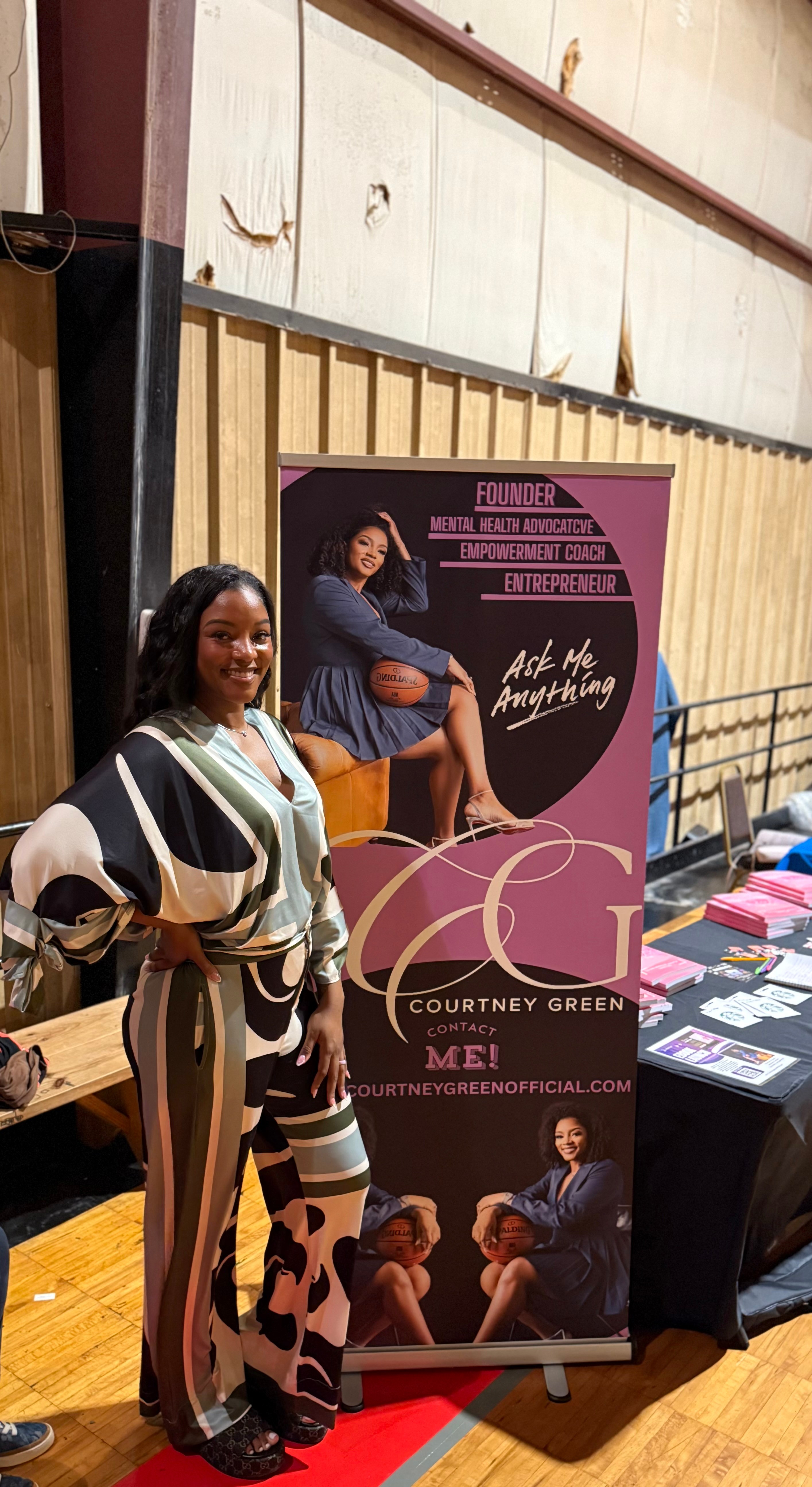 Woman standing next to a promotional banner for Courtney Green, featuring images of women and text, in an indoor setting.