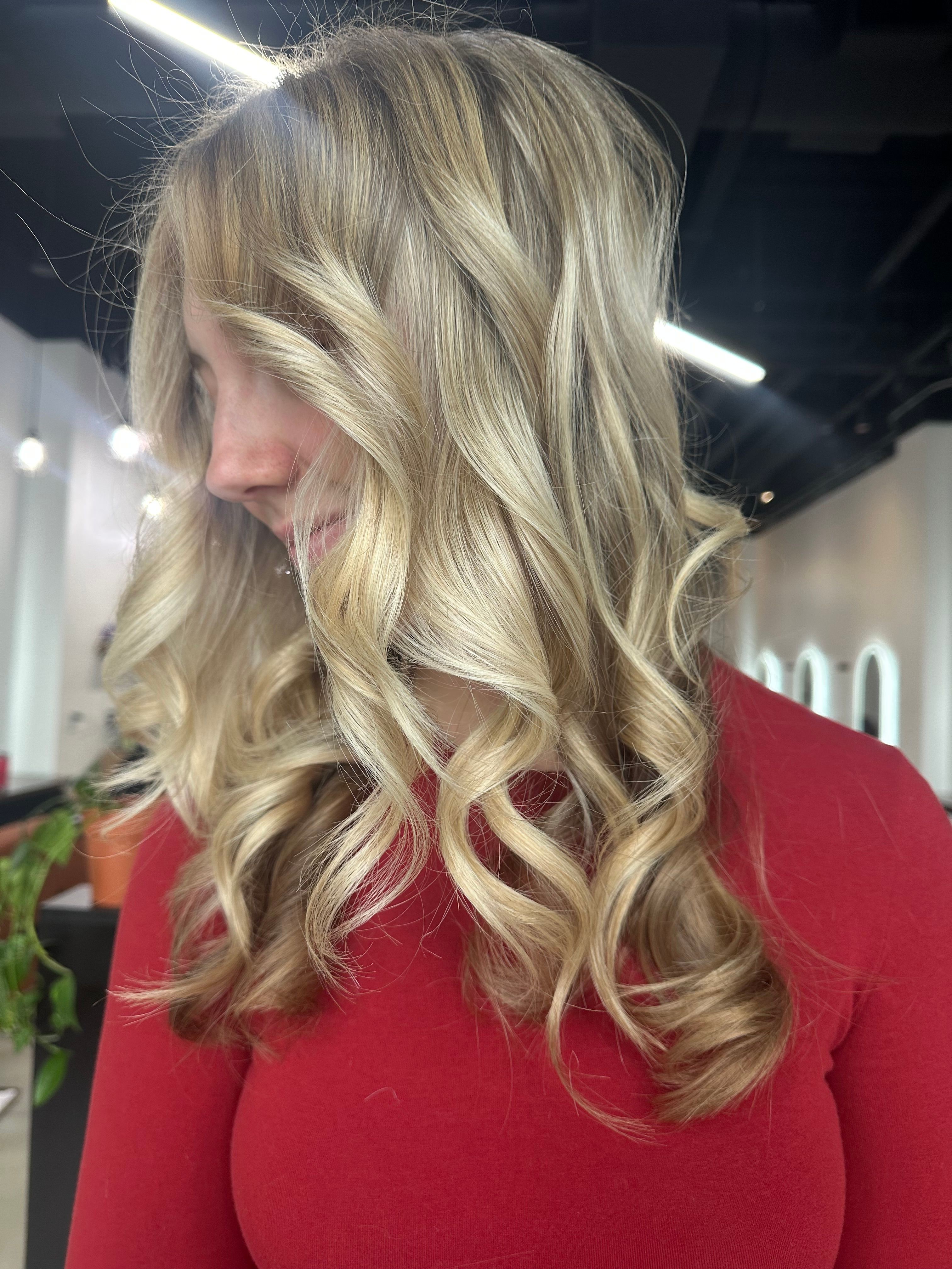 Side view of a woman with long, wavy blonde hair wearing a red top, indoors with bright lighting.