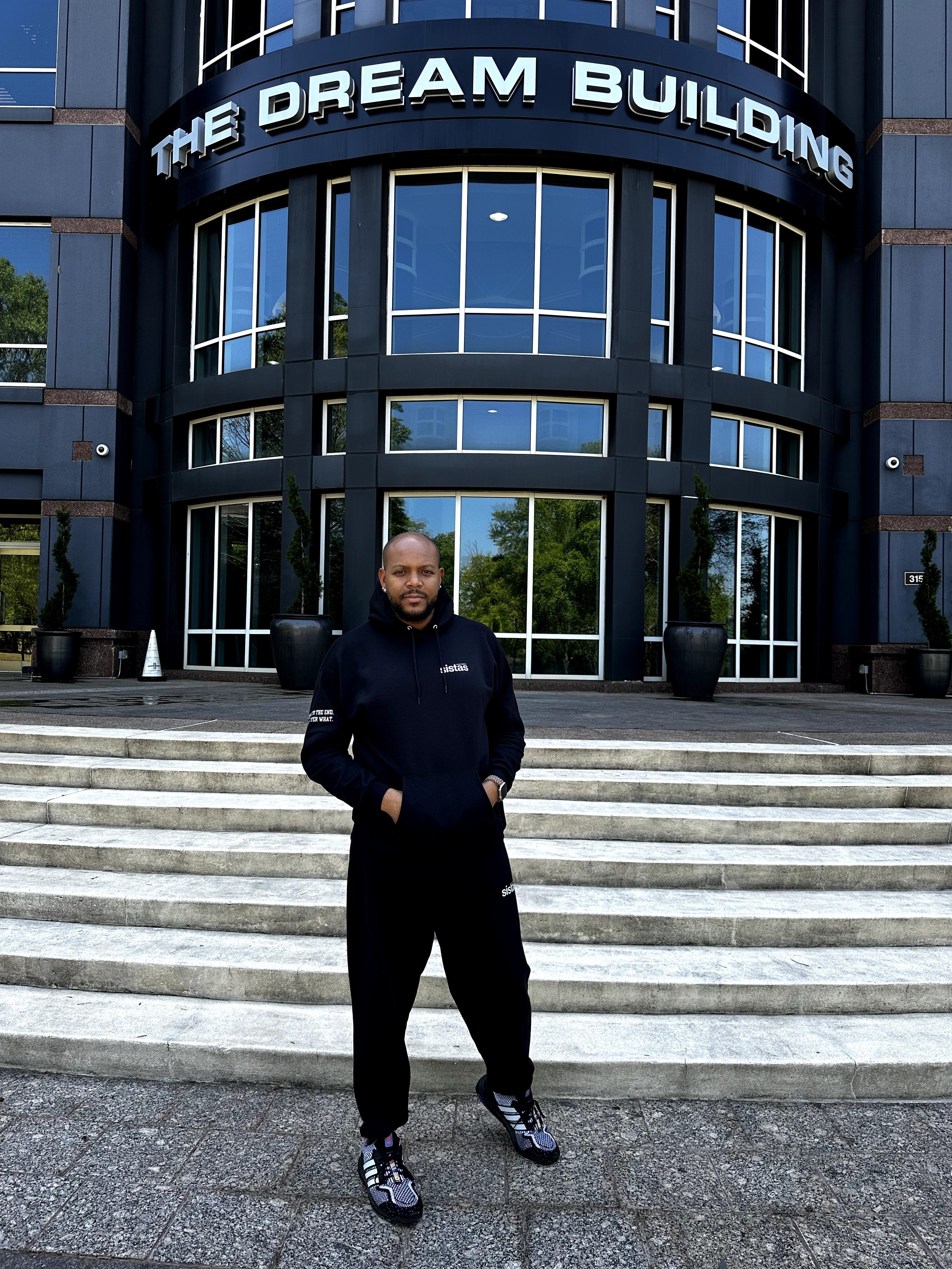 Person standing on steps in front of a building with a sign reading 'The Dream Building'.