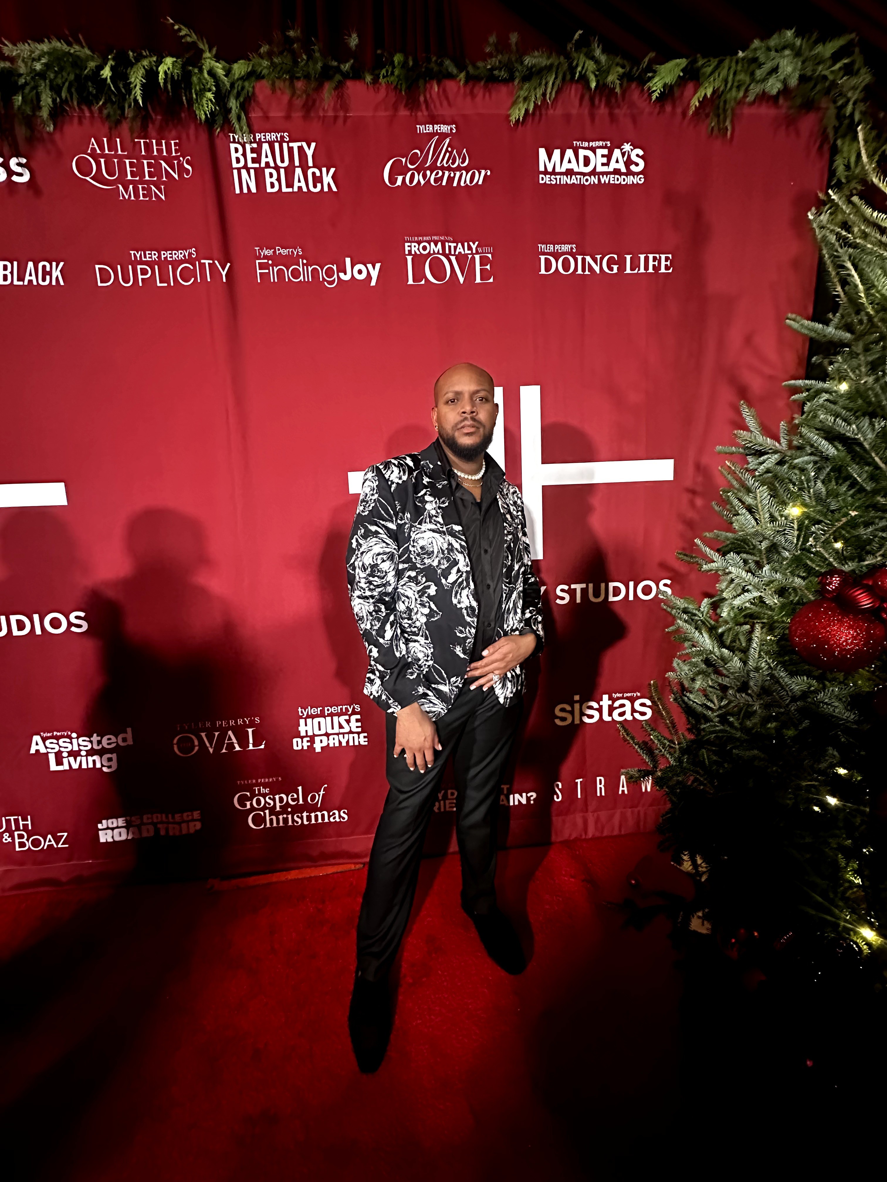 Man standing in front of a red backdrop with various white text and logos, next to a decorated Christmas tree.