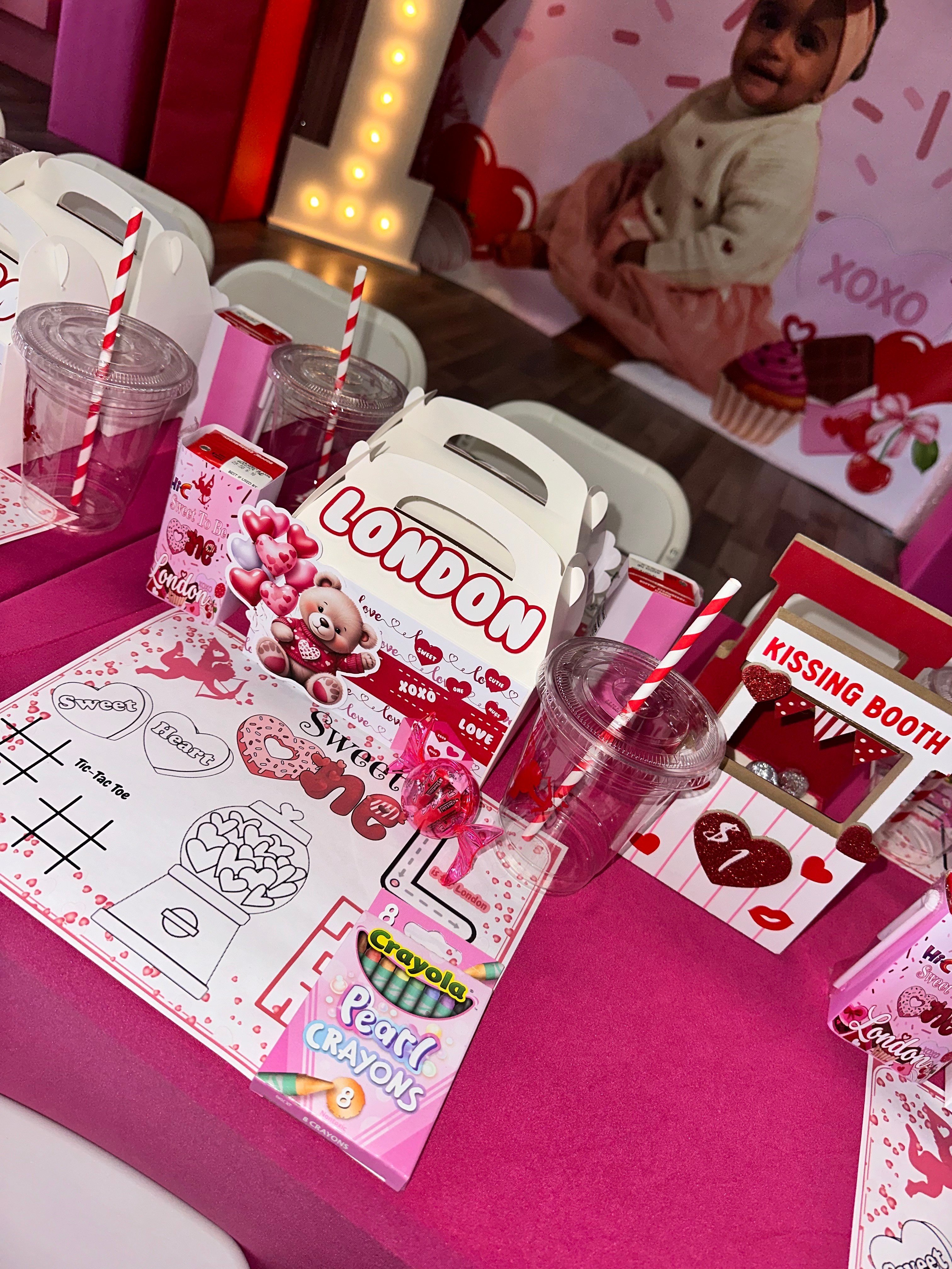 Party table with pink decorations, cups, and a poster of a baby girl, celebrating a birthday.