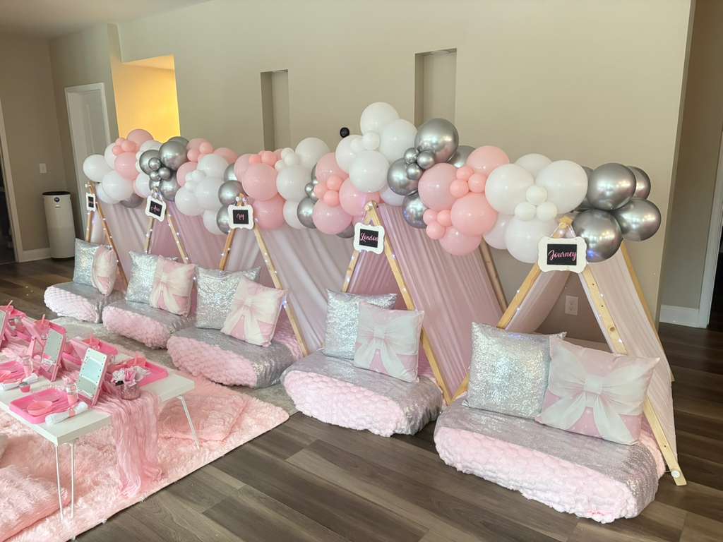 Decorative backdrop with pink, white, and silver balloons, and wooden structures, set against a wall with small rectangular cutouts.