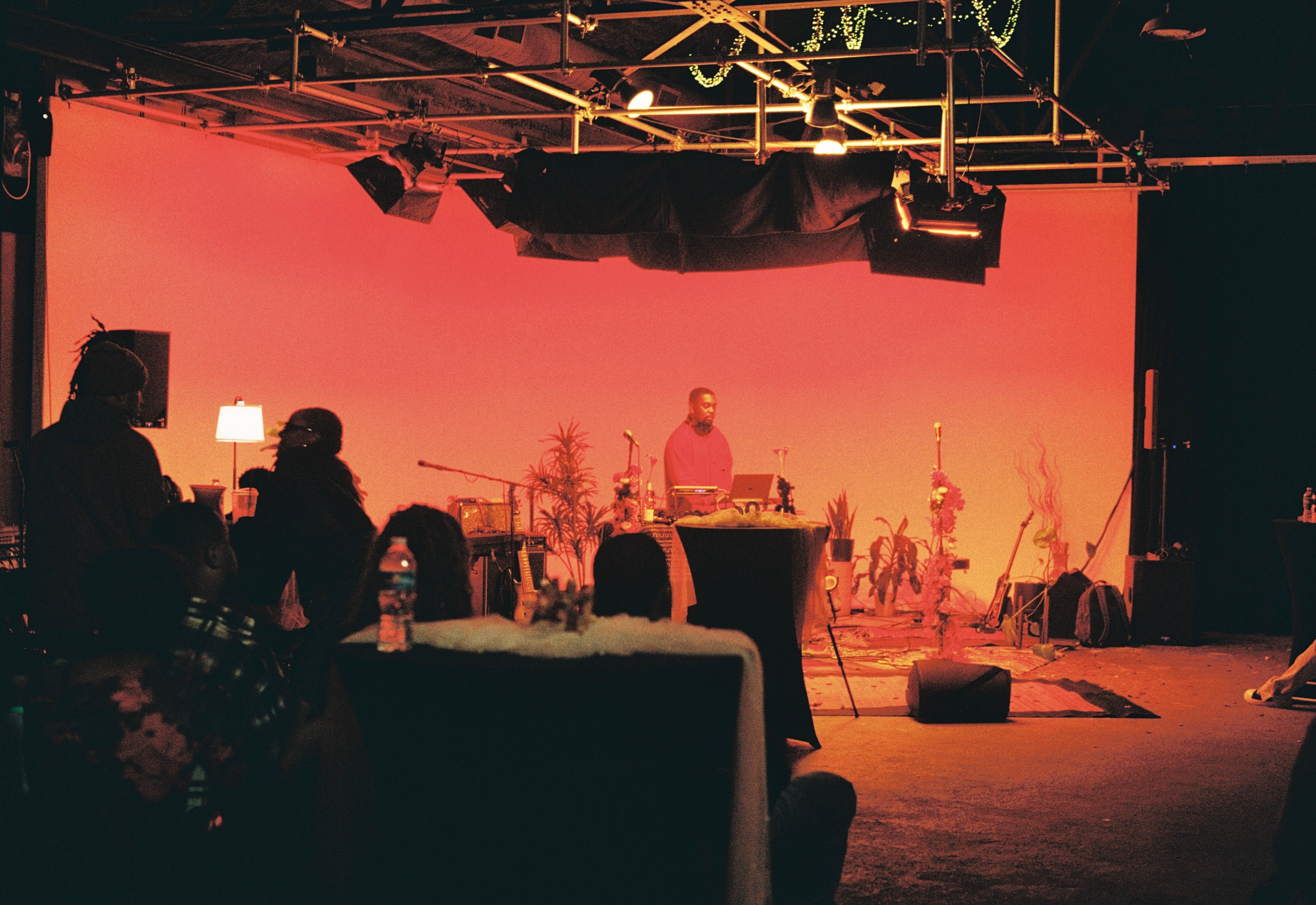 People watching a performer on stage with pink background, stage lights, and musical instruments, in a dimly lit venue.
