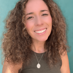 Smiling woman with curly hair wearing a dark top and necklace, against a teal background.