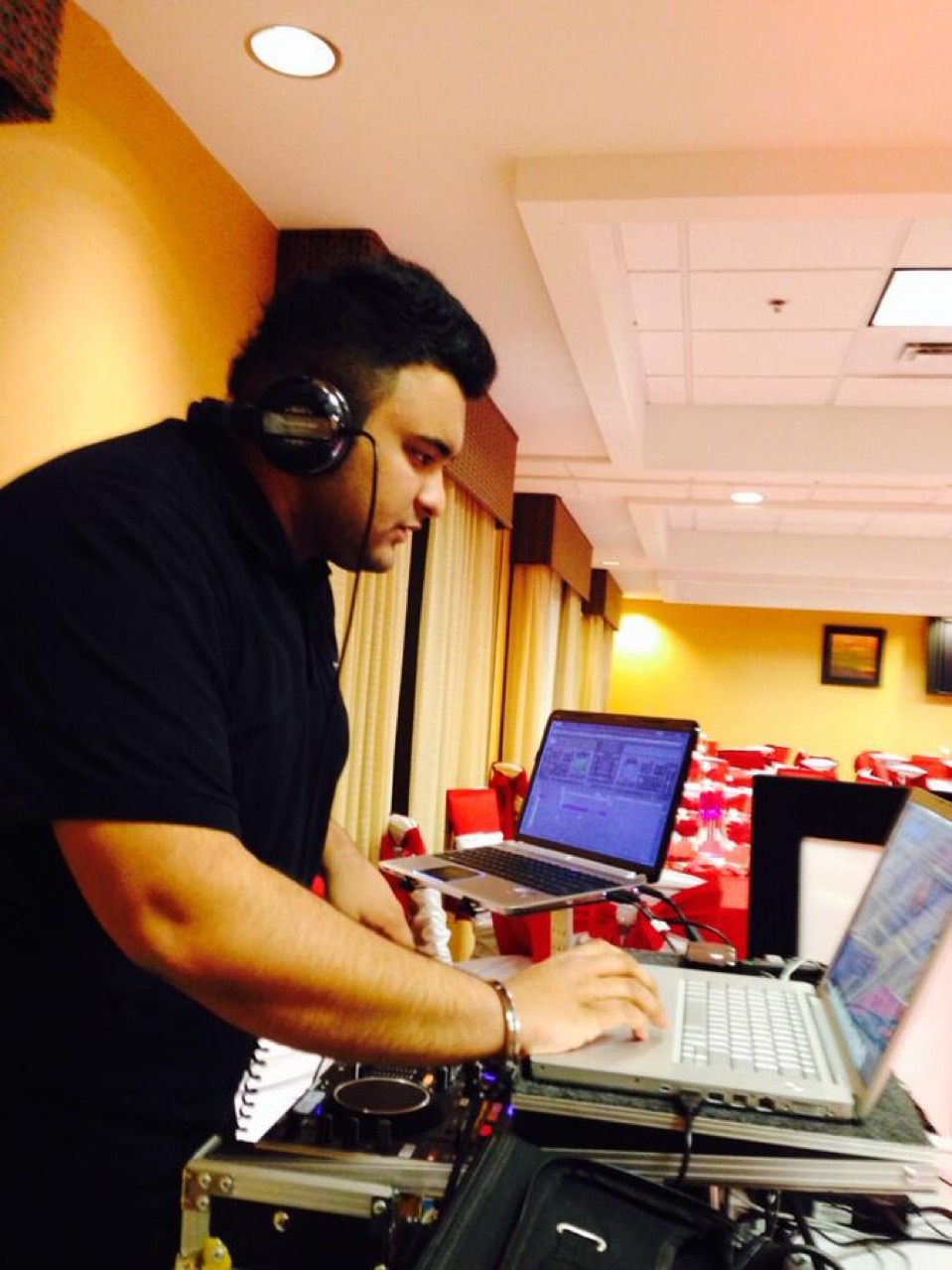 Man with headphones working on a laptop in a room with yellow walls and red chairs.