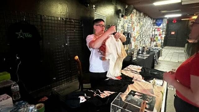 Person holding a large cloth or garment in a room with tables and equipment, possibly a store or event space.