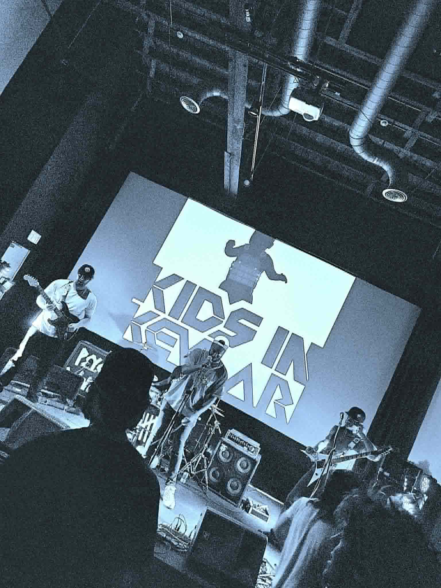 Stage with band performing and a large screen displaying a silhouette of a child jumping, with text 'Kids in Motion'.