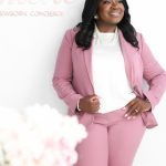 Woman in pink suit smiling, standing with hands on hips, white background with pink text, blurred flowers in foreground.