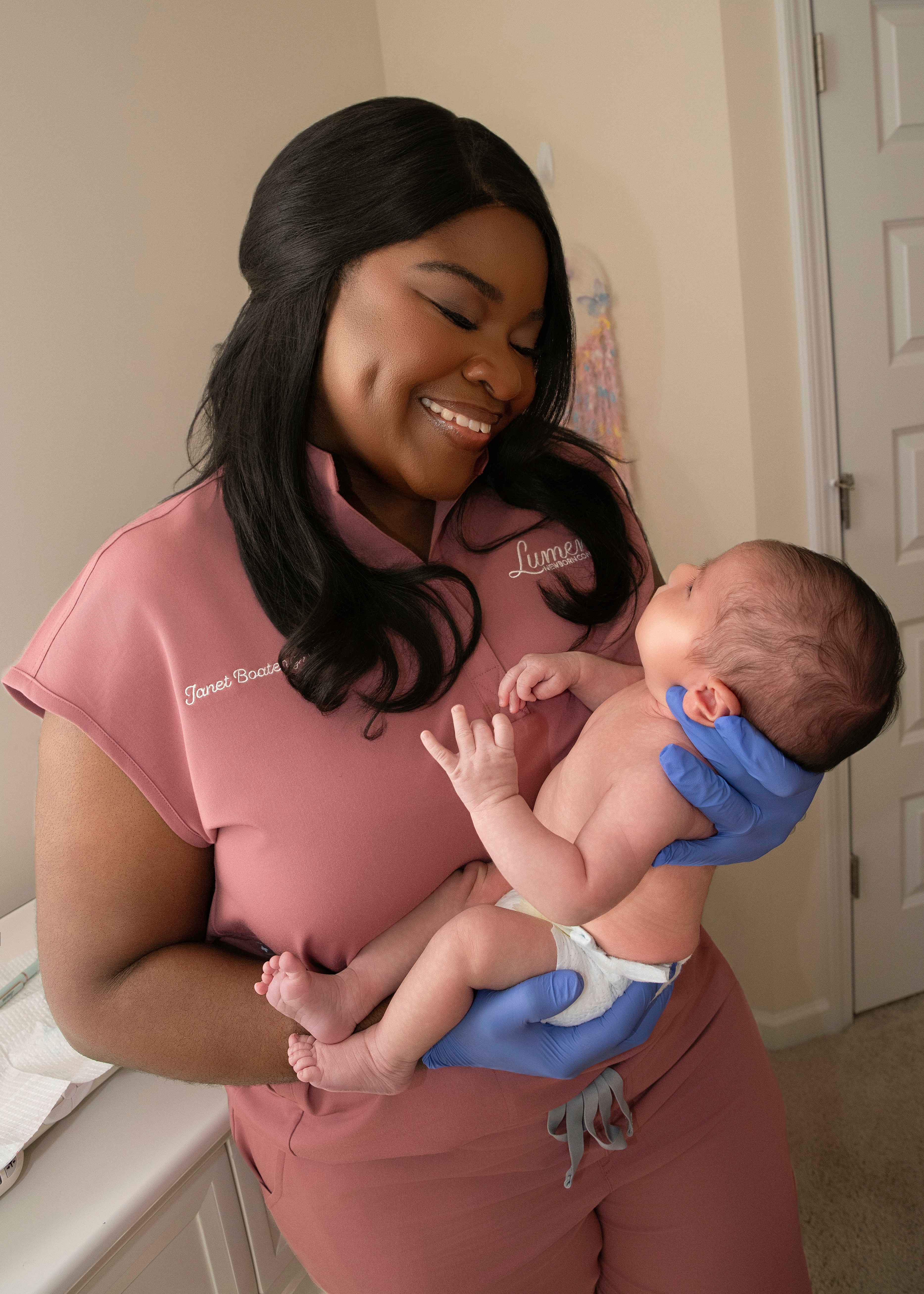 Woman holding a baby, smiling, in a room with a door in the background.