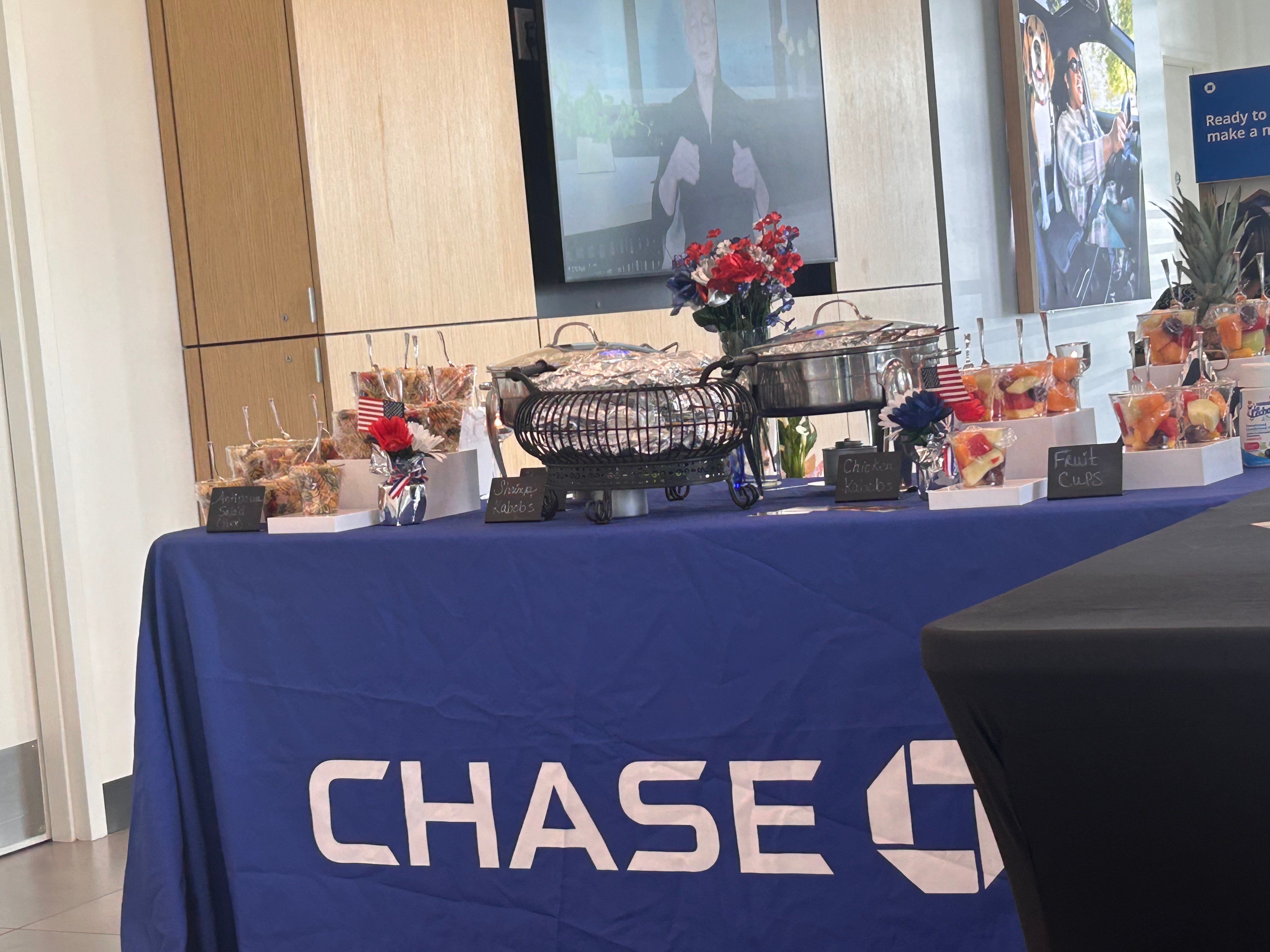 Table with snacks and drinks covered with a blue cloth, Chase logo visible, in a room with wooden paneling and screens.